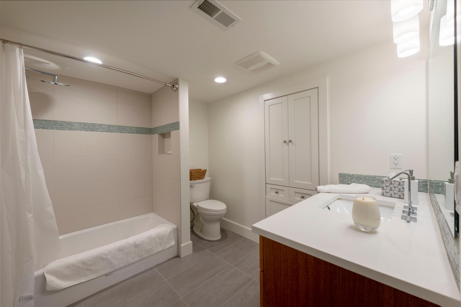 Bathroom featuring a tiled tub-shower combination with an accent mosaic border, a built-in shower niche, a single vanity with a white countertop and rectangular undermount sink, and a tall built-in storage cabinet