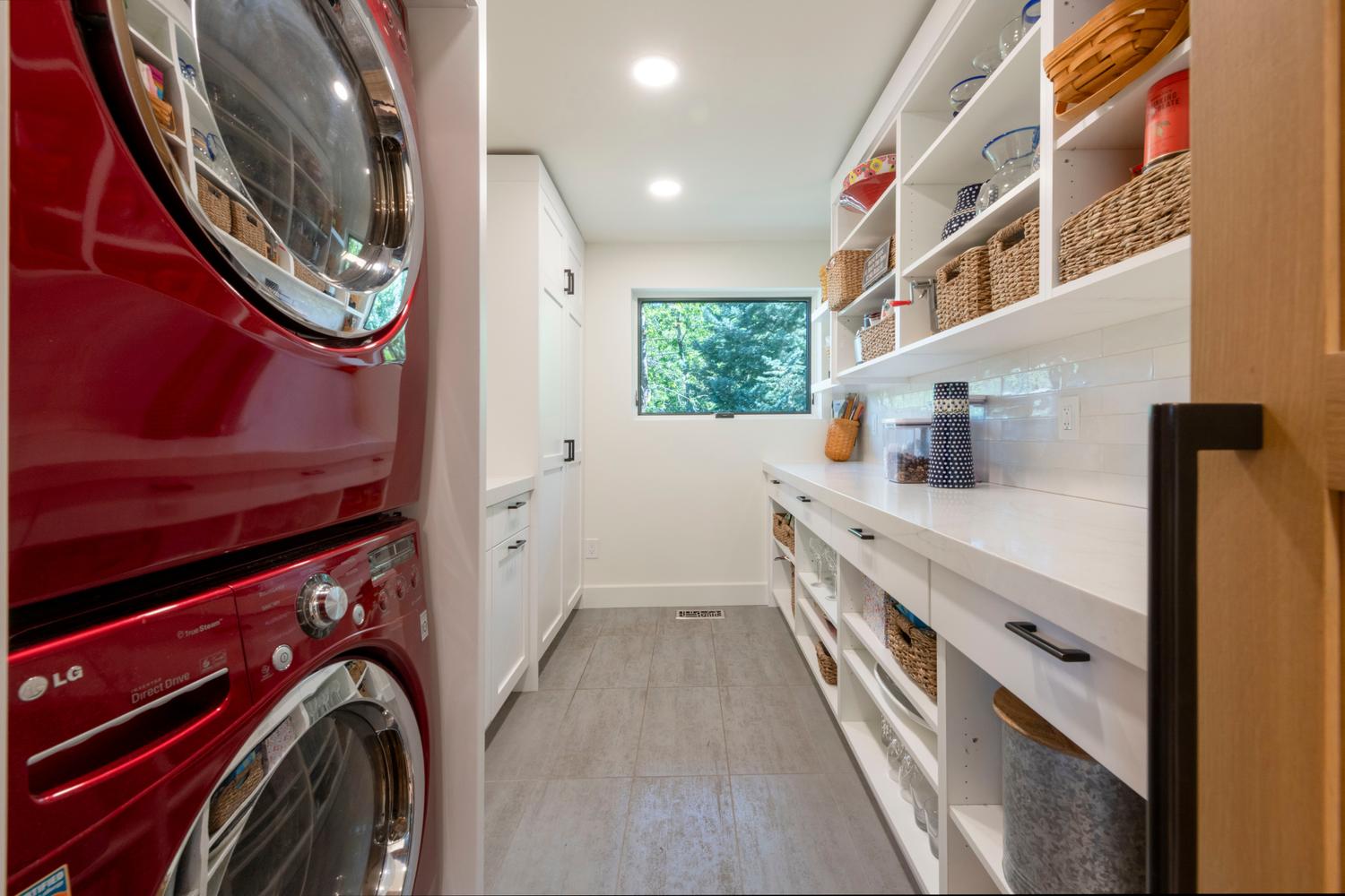 Dedicated laundry and pantry area featuring stacked red appliances, extensive built-in white shelving, white countertops, a subway tile backsplash, and recessed lighting