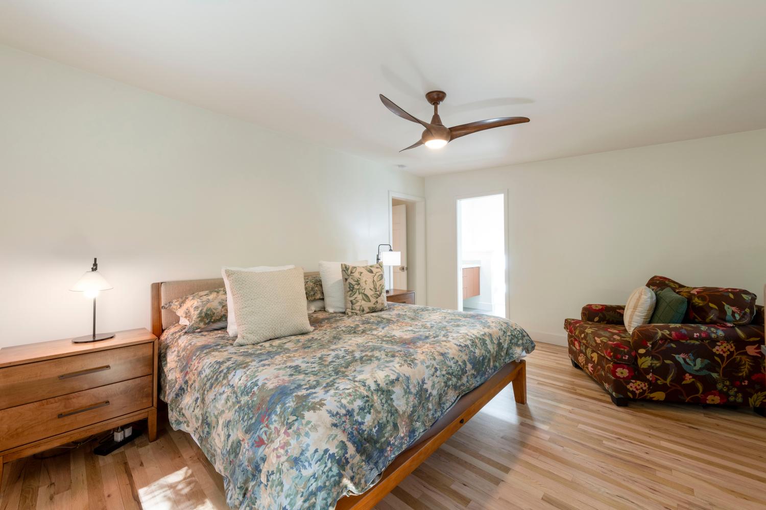 Spacious bedroom featuring light wood-finish flooring, a contemporary ceiling fan with integrated lighting, and a light-filled doorway leading to another room