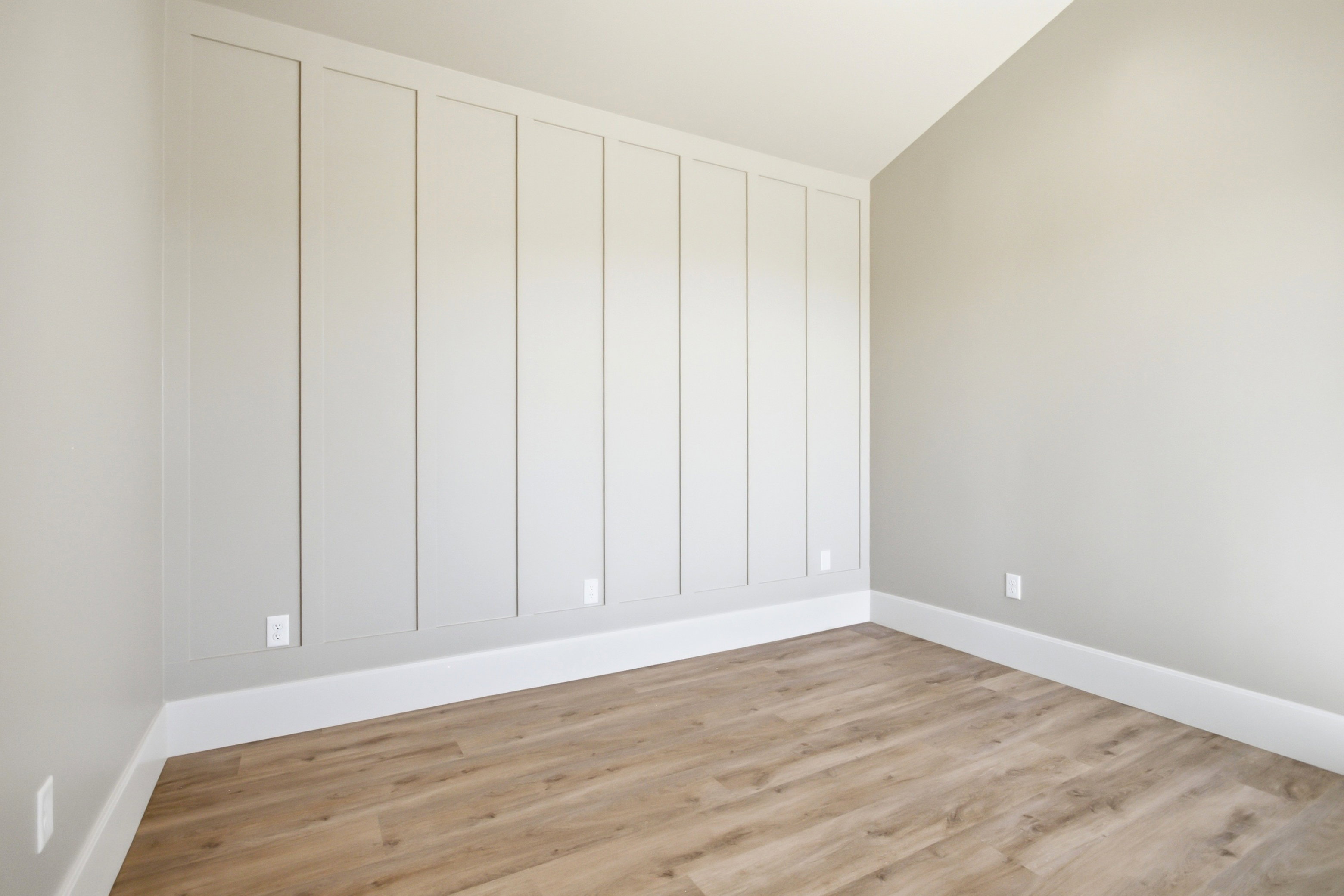 Accent wall featuring vertical paneling, crisp white baseboards, and neutral wall paint