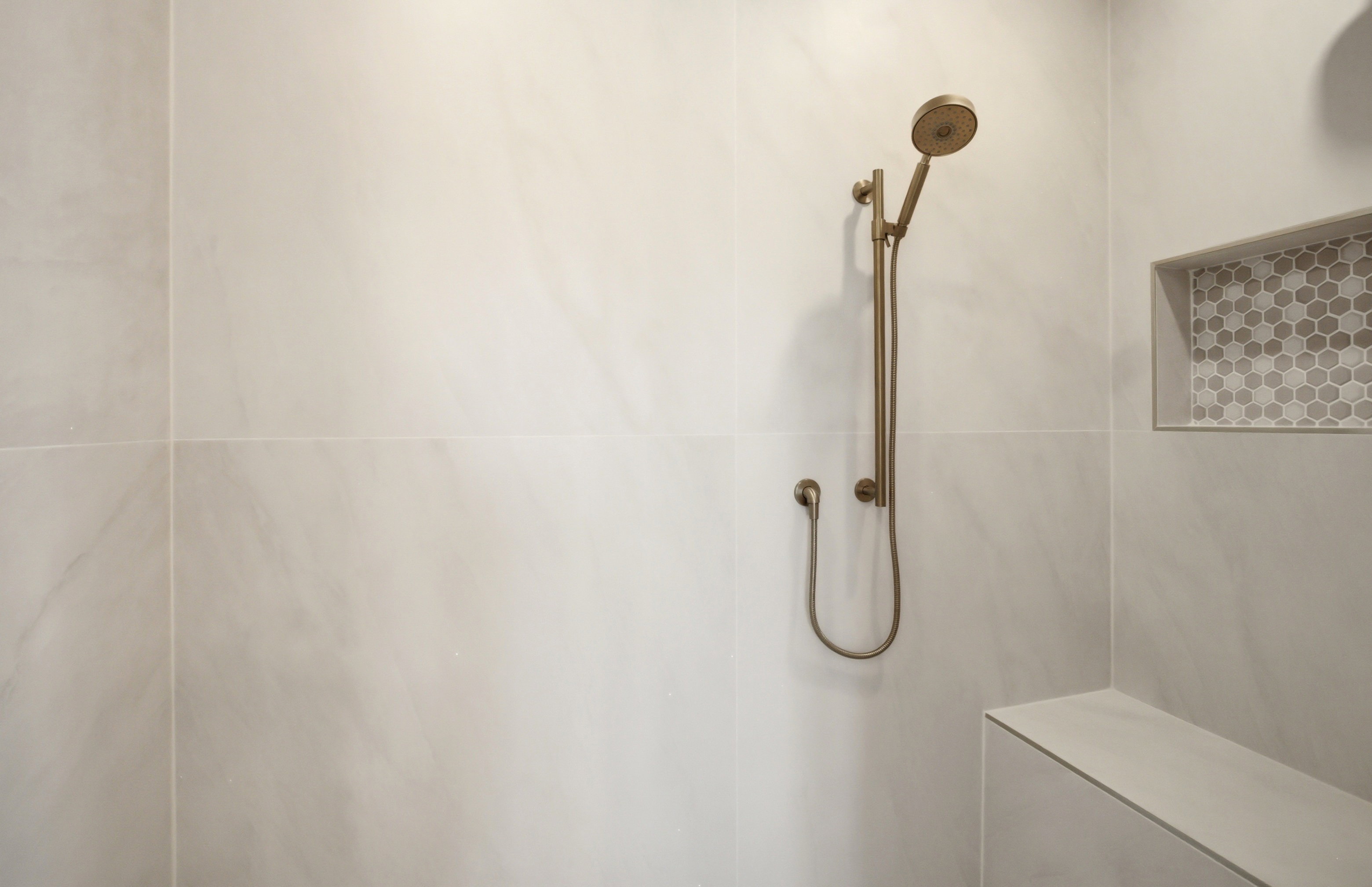 Shower featuring large format wall tiling, a built-in bench, and a recessed niche with mosaic hexagon tile
