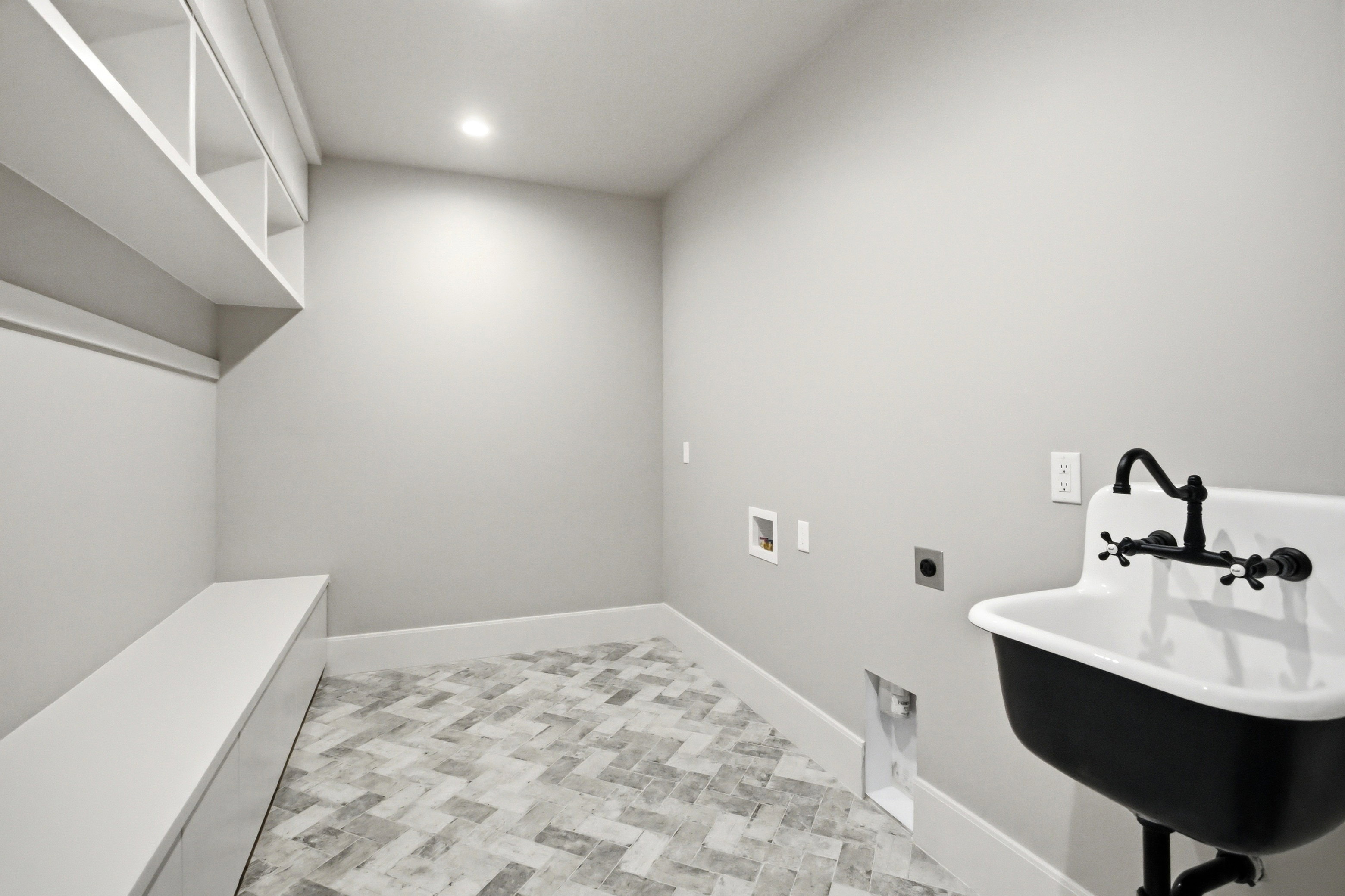Utility room featuring herringbone pattern tile flooring, recessed lighting, built-in shelving, a storage bench, and a wall-mounted utility sink with a black faucet