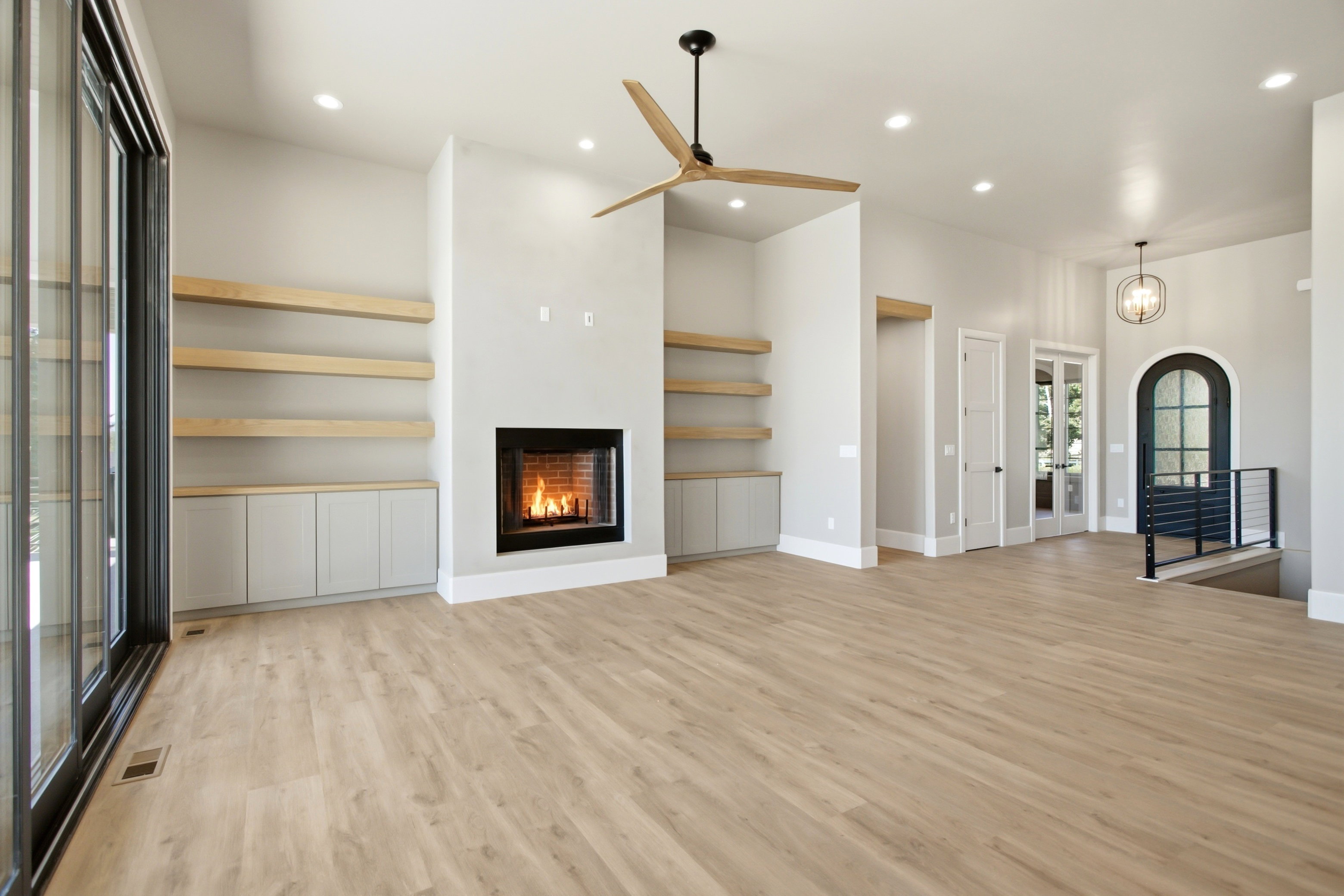 Spacious open-concept room featuring a contemporary fireplace, custom built-in shelving with lower cabinetry, recessed lighting, and a large sliding glass door