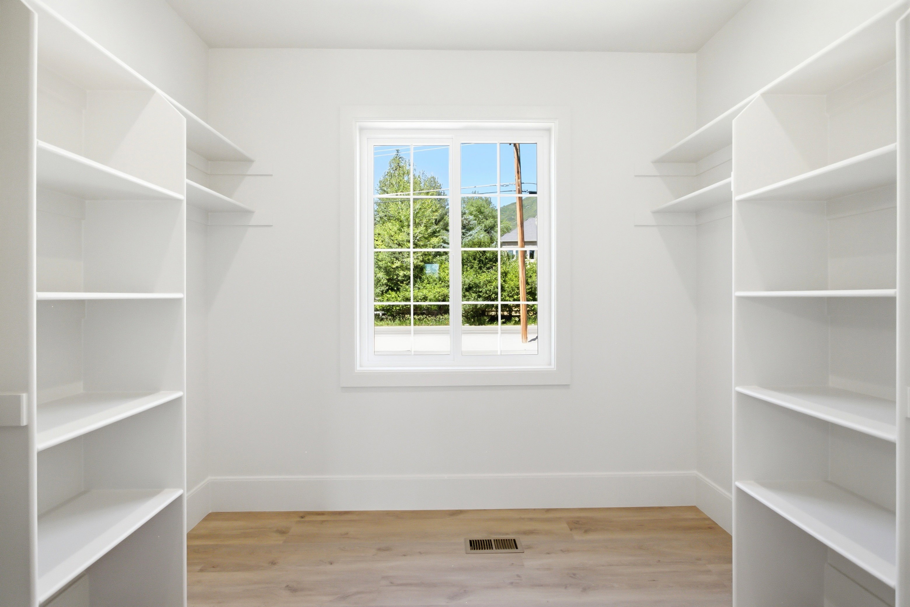 Walk-in closet featuring white built-in shelving, light wood-finish flooring, and a central window providing natural illumination