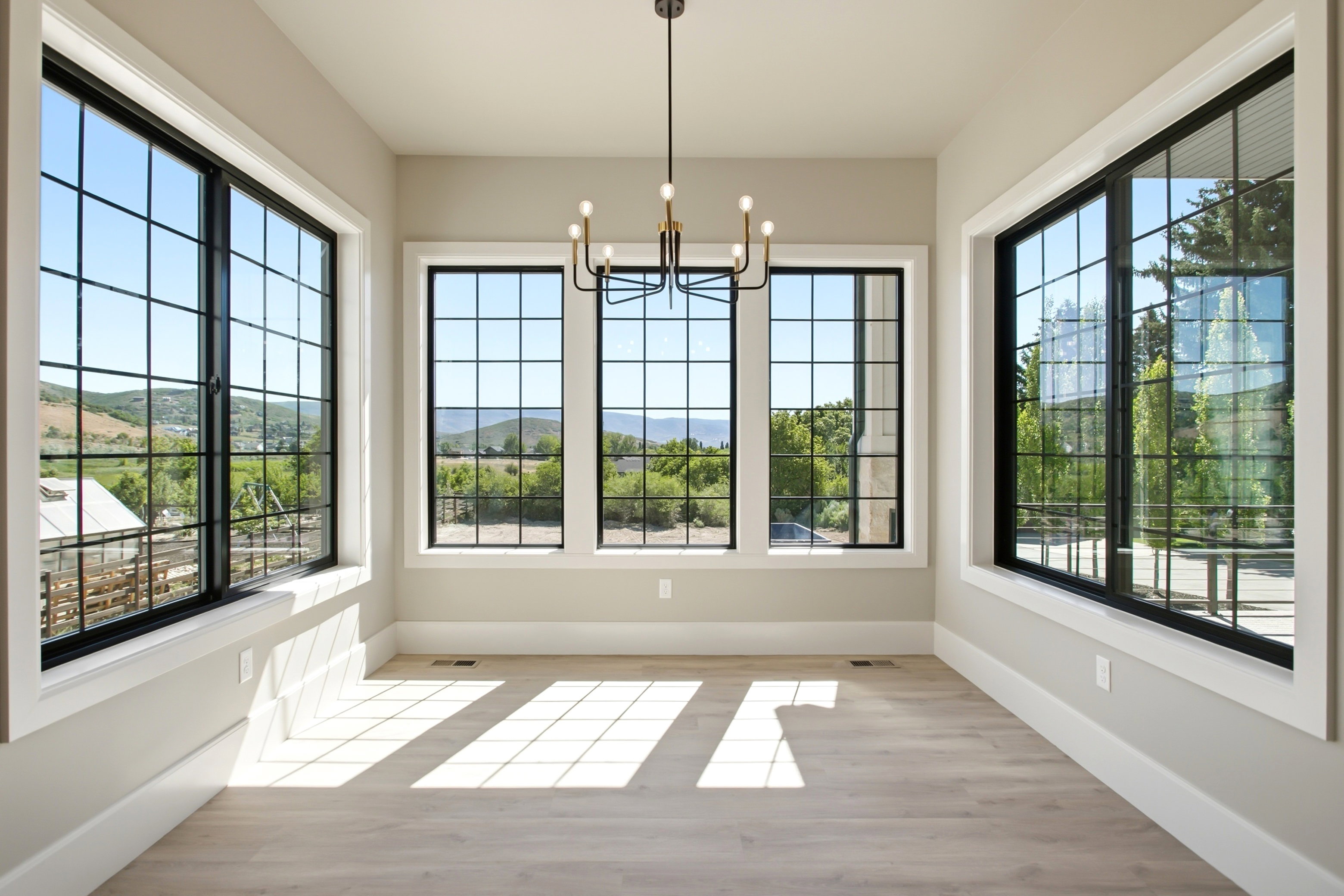 Spacious dining room featuring a contemporary black and gold chandelier, and multiple large black-framed windows with grid patterns