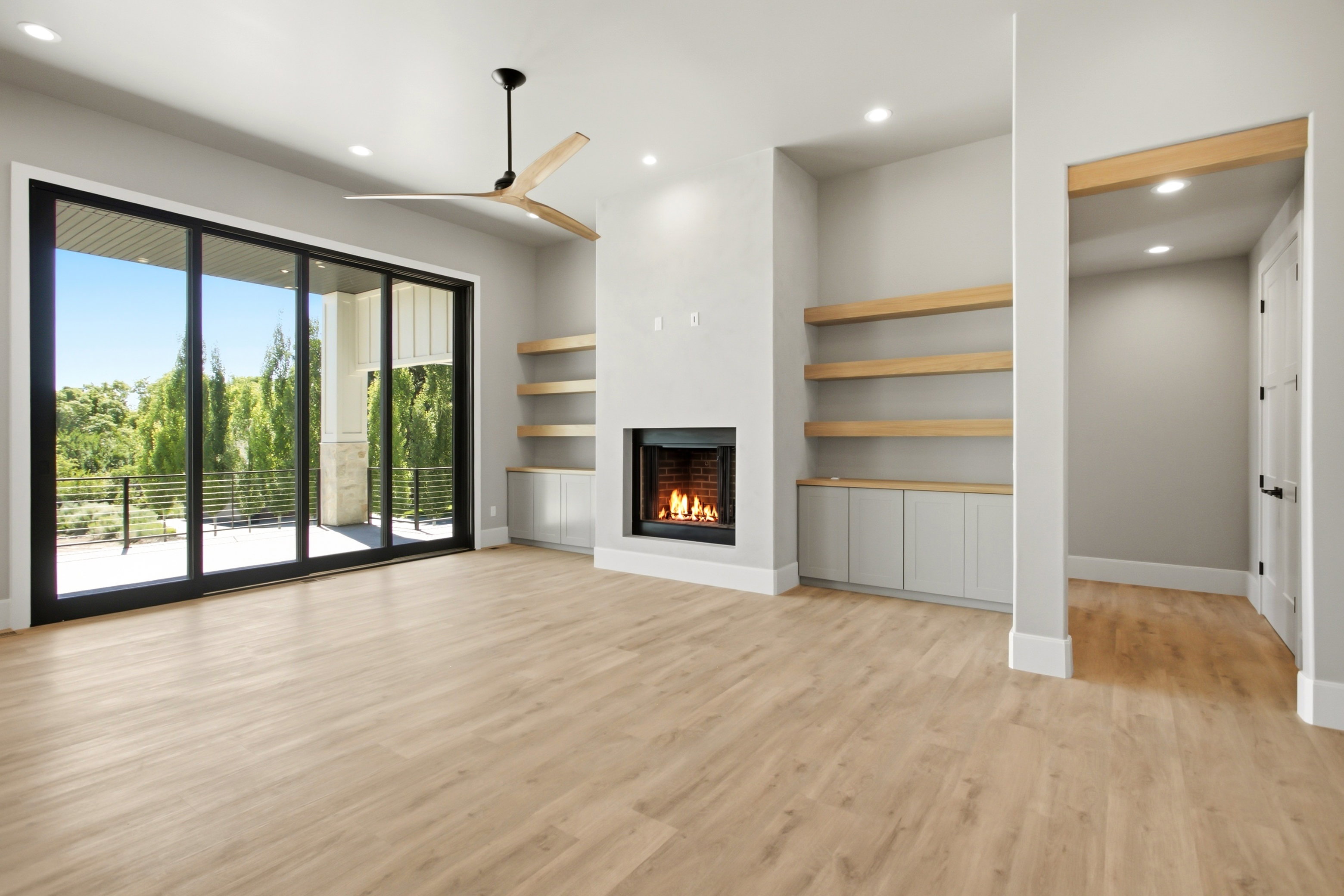 Spacious living area featuring expansive sliding glass doors, a contemporary fireplace, built-in shelving with base cabinetry, and a modern ceiling fan
