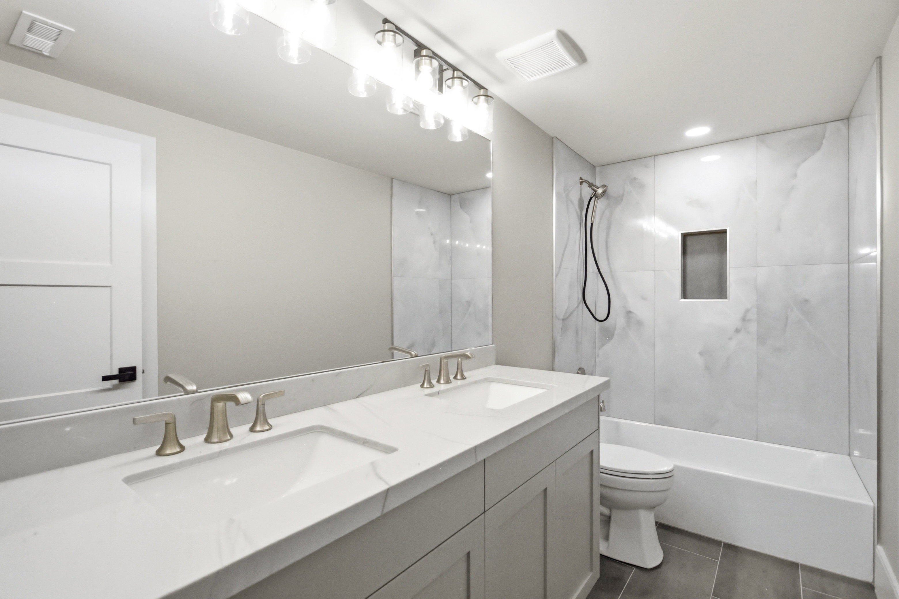 Bathroom featuring a dual-sink vanity with white countertops, brushed nickel faucets, and a full-width mirror