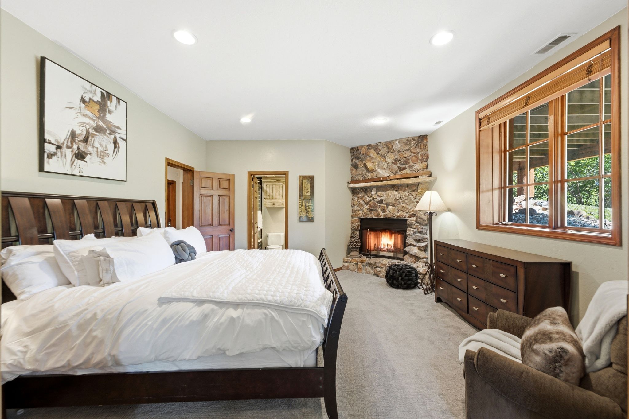 Spacious room featuring a corner stone fireplace, wood-framed windows, recessed lighting, and light-toned carpeting
