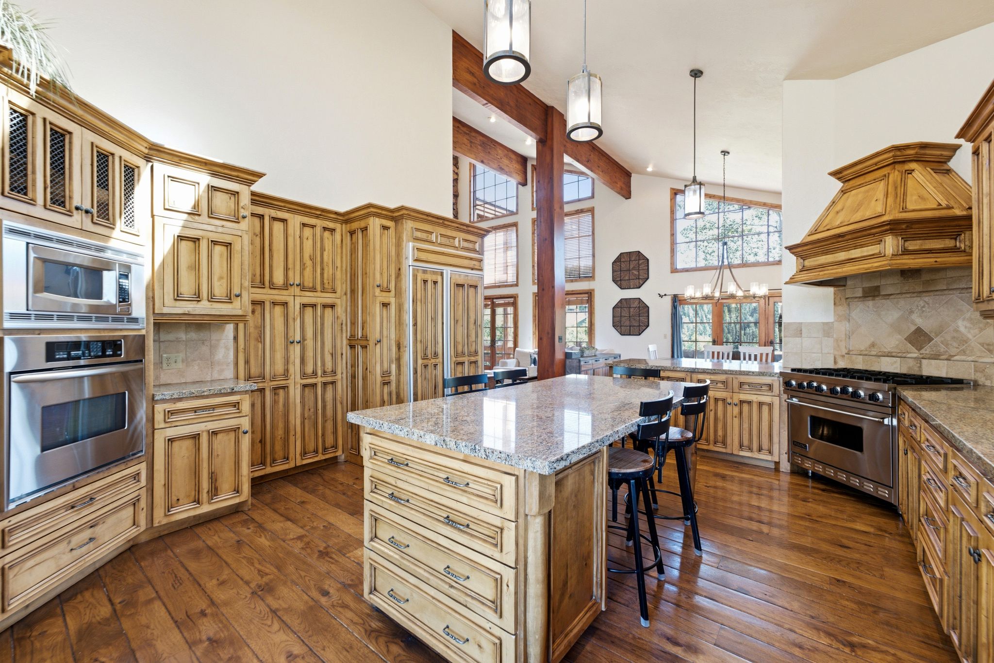 Spacious kitchen featuring custom wood cabinetry, stainless steel appliances, a large island with a stone countertop, and wood-finish flooring