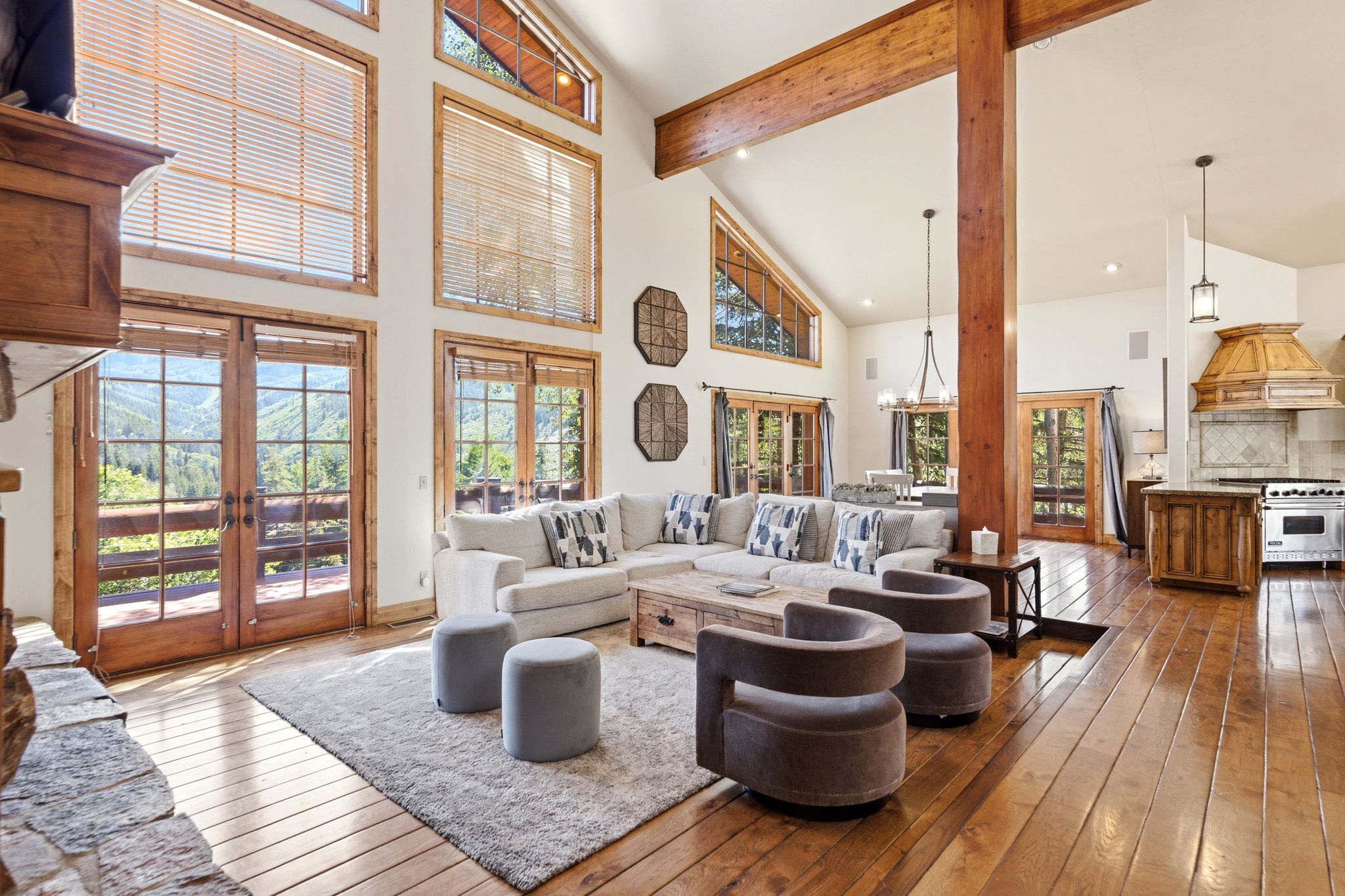 Great room featuring vaulted ceilings, exposed wood beams, hardwood flooring, a stone-front fireplace, and French doors opening to outdoor scenery