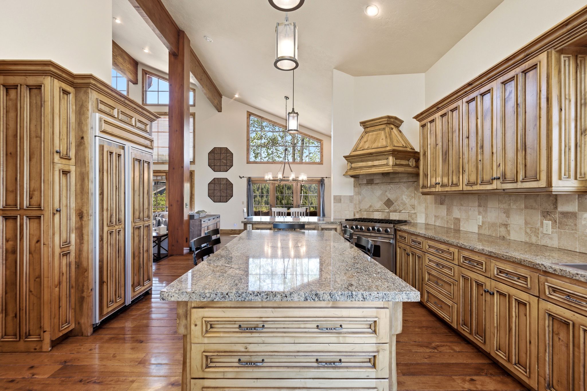 Spacious kitchen featuring an expansive center island, granite countertops, custom wood cabinetry, stainless steel range, and stone tile backsplash