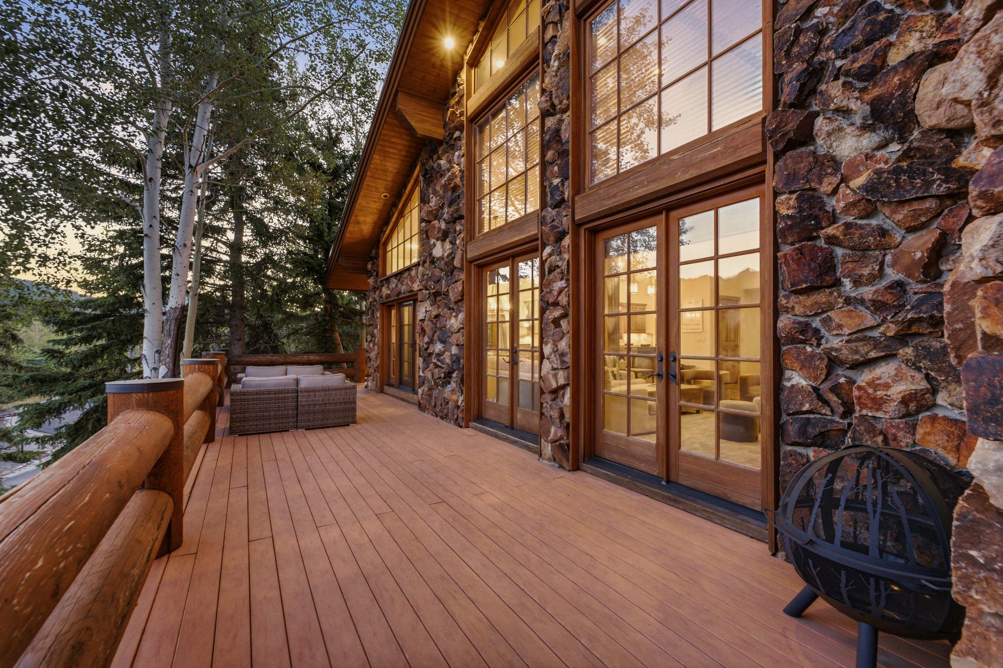 Expansive wood-finish deck with log railing, featuring multiple sets of glass-paneled French doors and a stone exterior