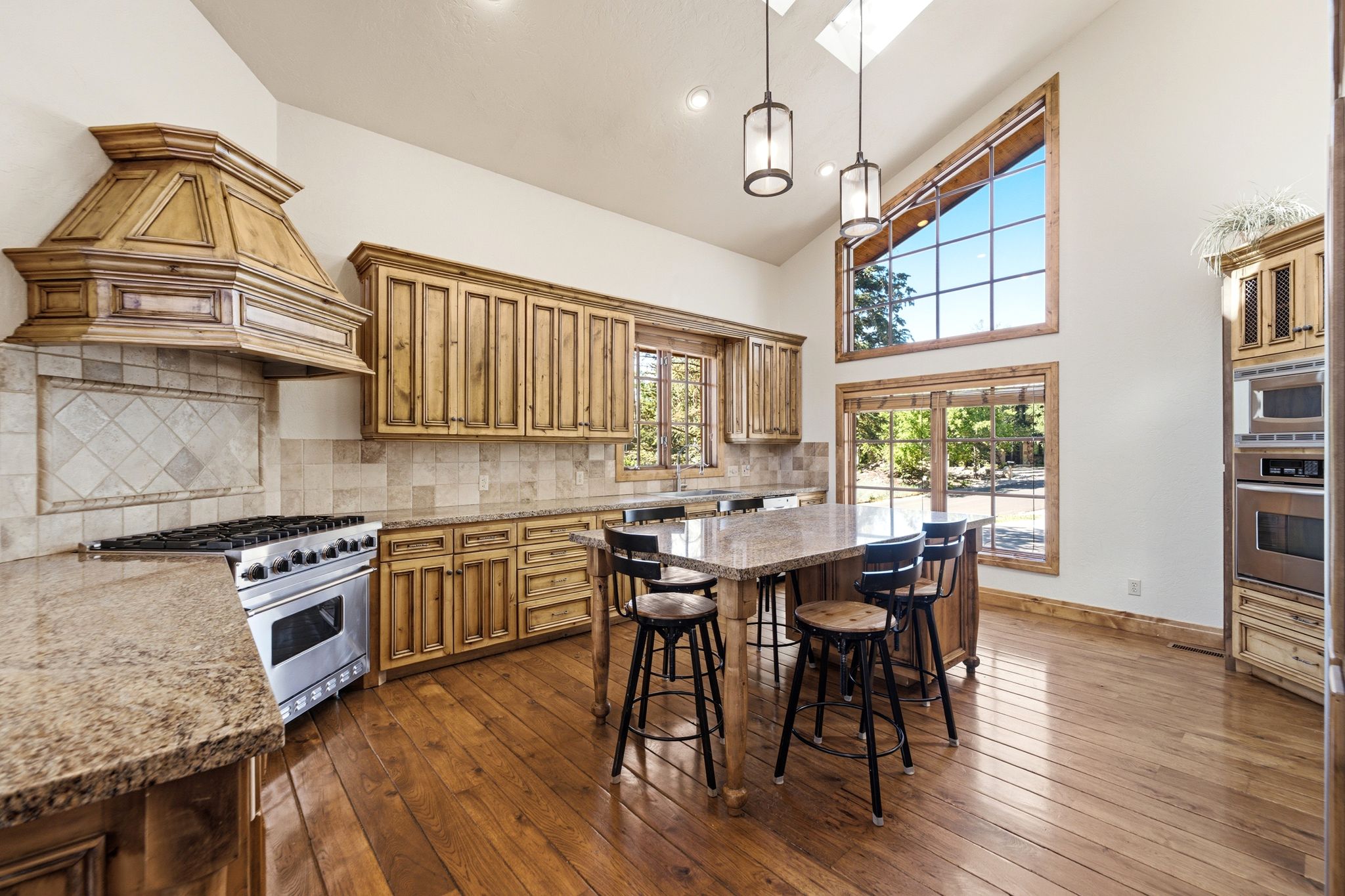 Vaulted kitchen featuring a custom wood range hood, a stainless-steel gas range, and wood-finish cabinetry