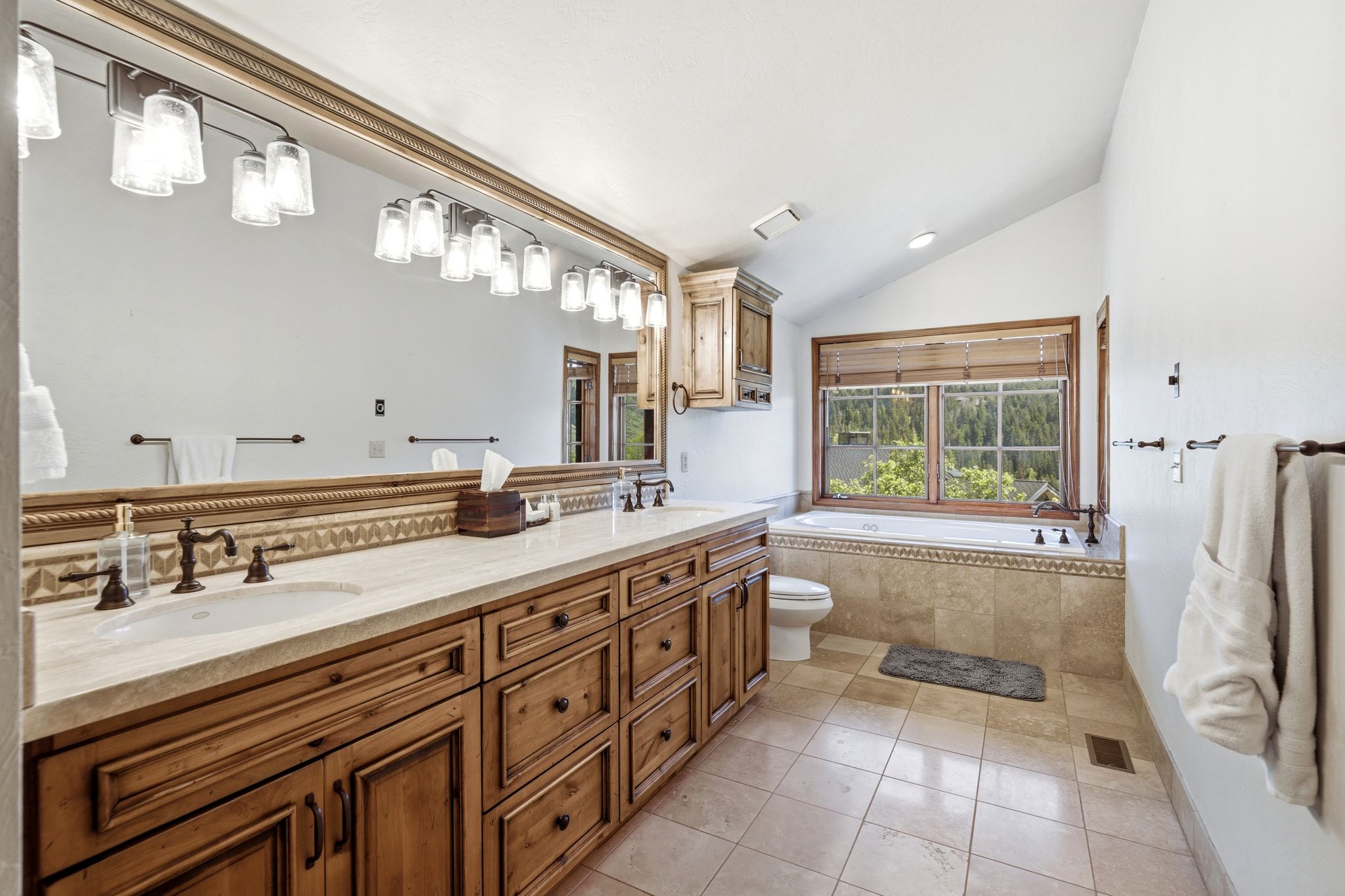 Dual vanity with bronze fixtures, light-toned countertop, and rich wood cabinetry