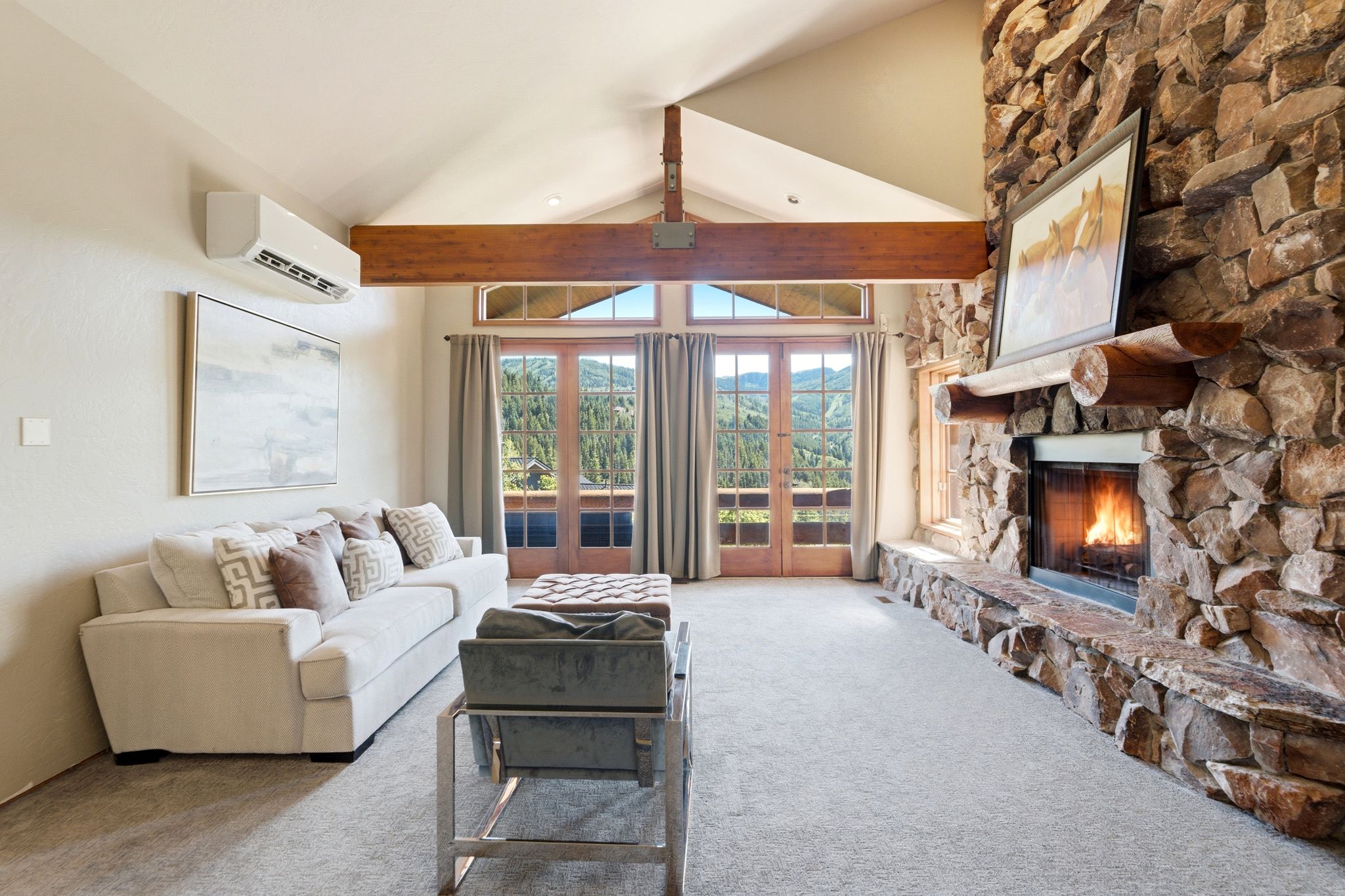 Vaulted ceilings with exposed wood beams, a full-height stone fireplace with a log mantel, and light-toned carpet flooring