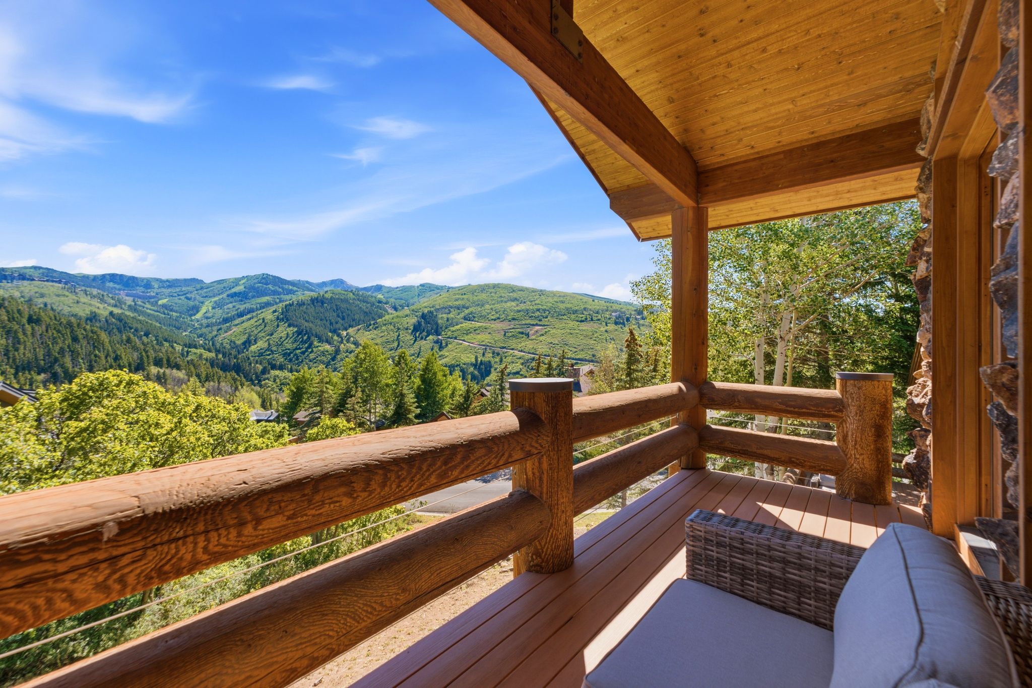 Covered outdoor deck with substantial log railing, wood-finish flooring, and a natural wood plank ceiling