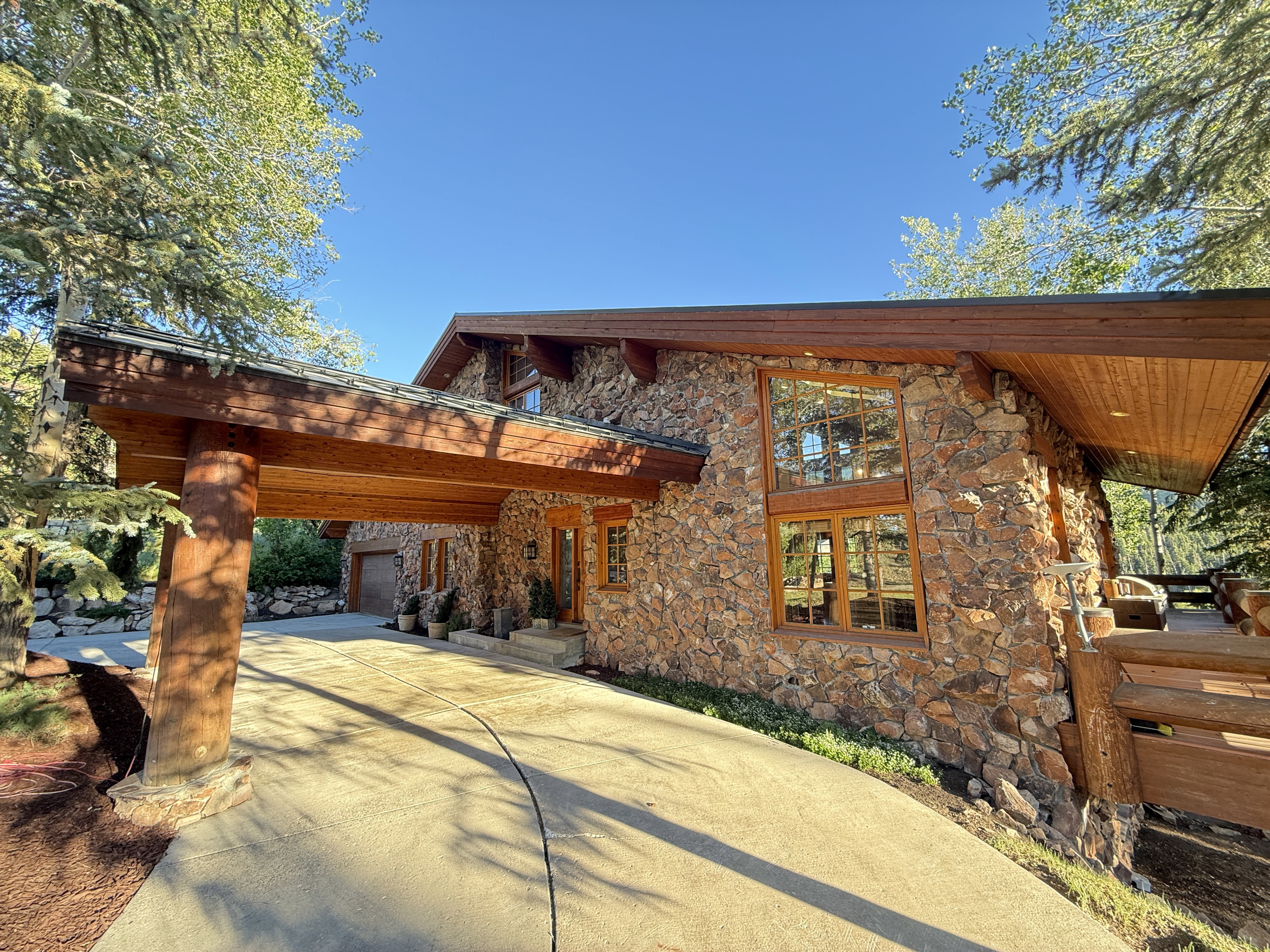 Stone exterior residence featuring a porte-cochère with log supports, extensive wood trim, large multi-pane windows, and a paved driveway