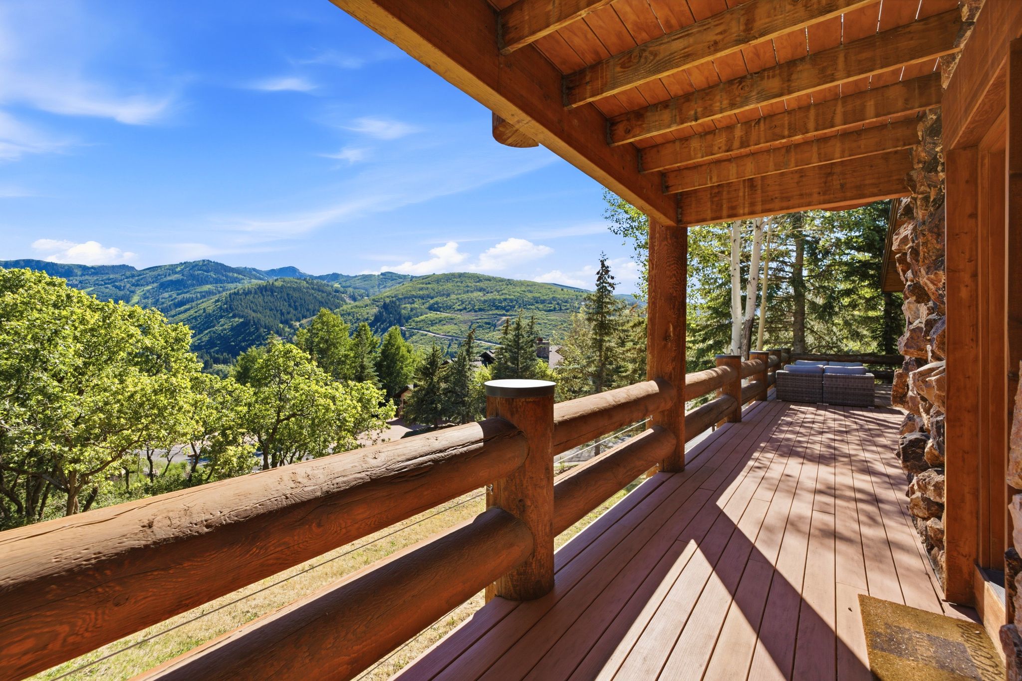 Expansive covered outdoor deck featuring wood plank flooring and log railing
