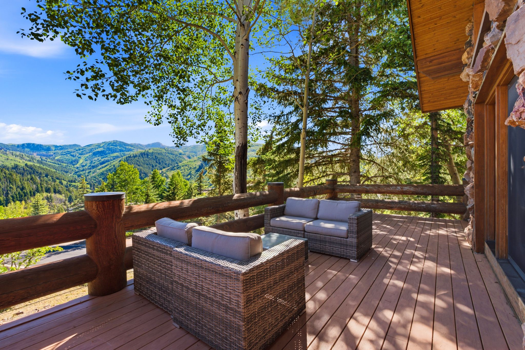 Expansive outdoor deck featuring wood-finish flooring, a rustic log railing, and a stone-clad exterior wall