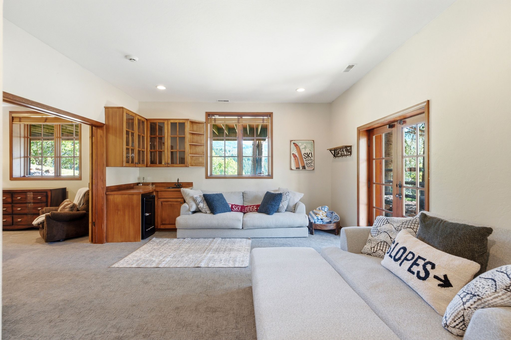 Carpeted recreation room featuring a built-in wet bar with wood cabinetry, glass-front upper cabinets, and an integrated beverage refrigerator