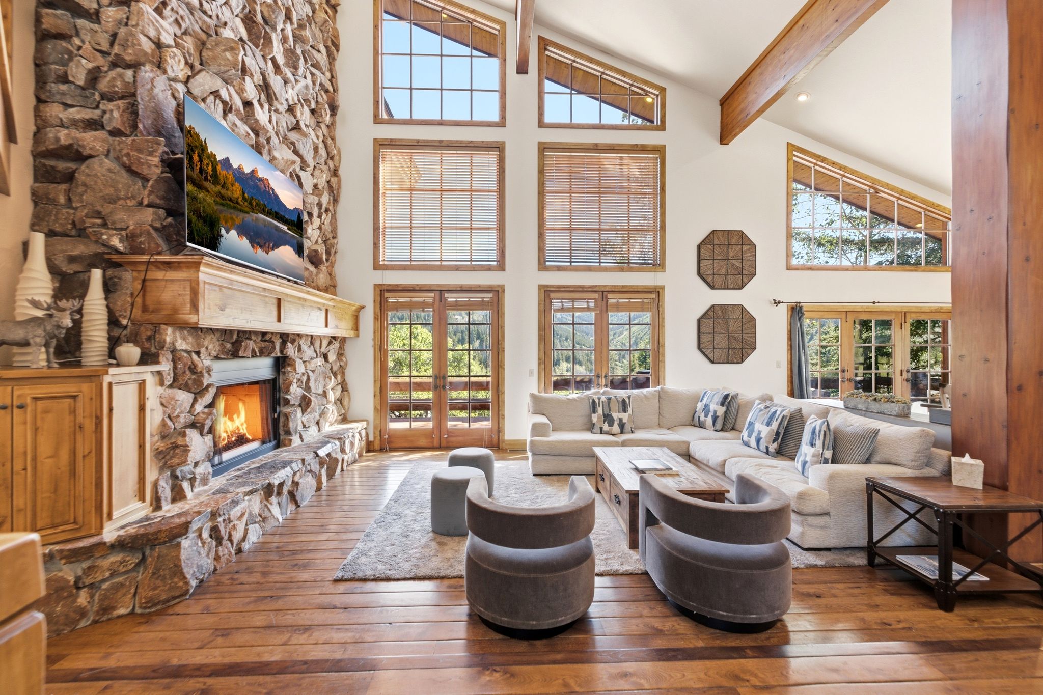 Vaulted living space featuring a floor-to-ceiling stone fireplace with a wood mantel, wood-finish flooring, and exposed wood beams