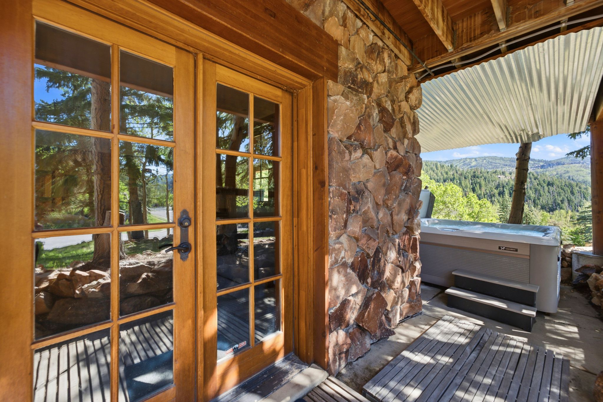 Stone patio with a built-in hot tub, wood-finish decking, and a corrugated metal awning