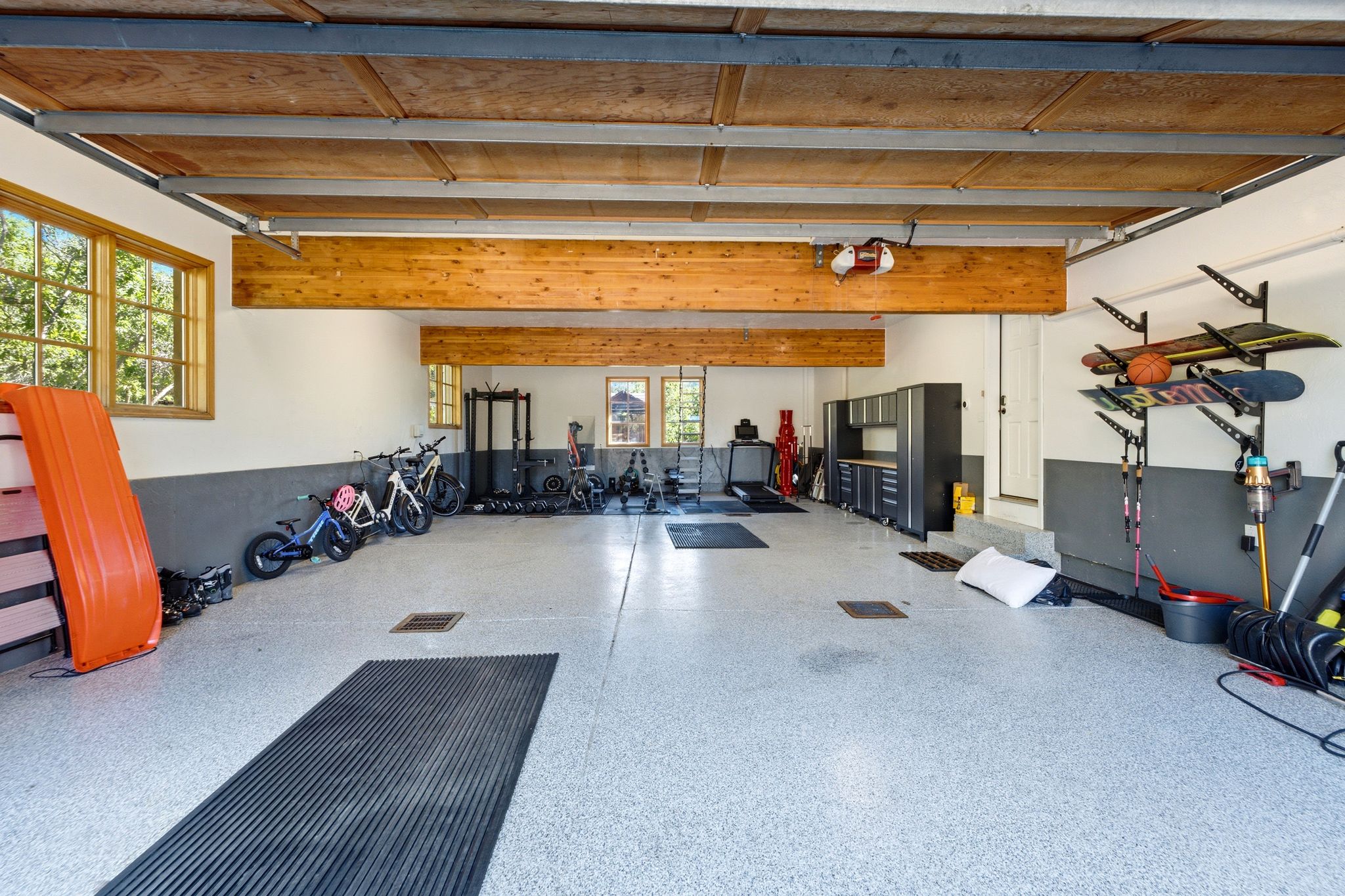 Spacious garage featuring a light epoxy flooring, light wood-finish ceiling, exposed wood beams, and multiple windows