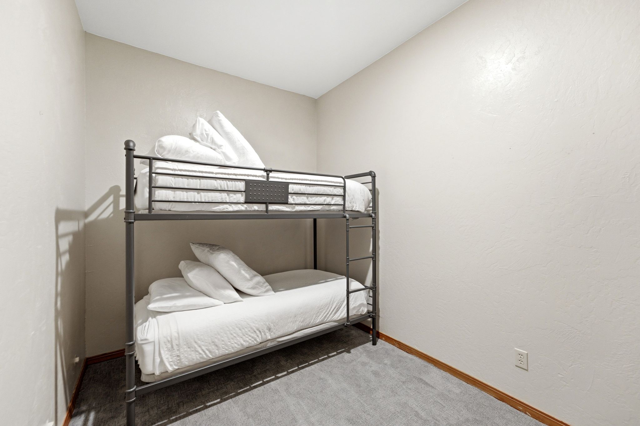 Compact room featuring a metal bunk bed frame, neutral-toned walls, and grey carpeting