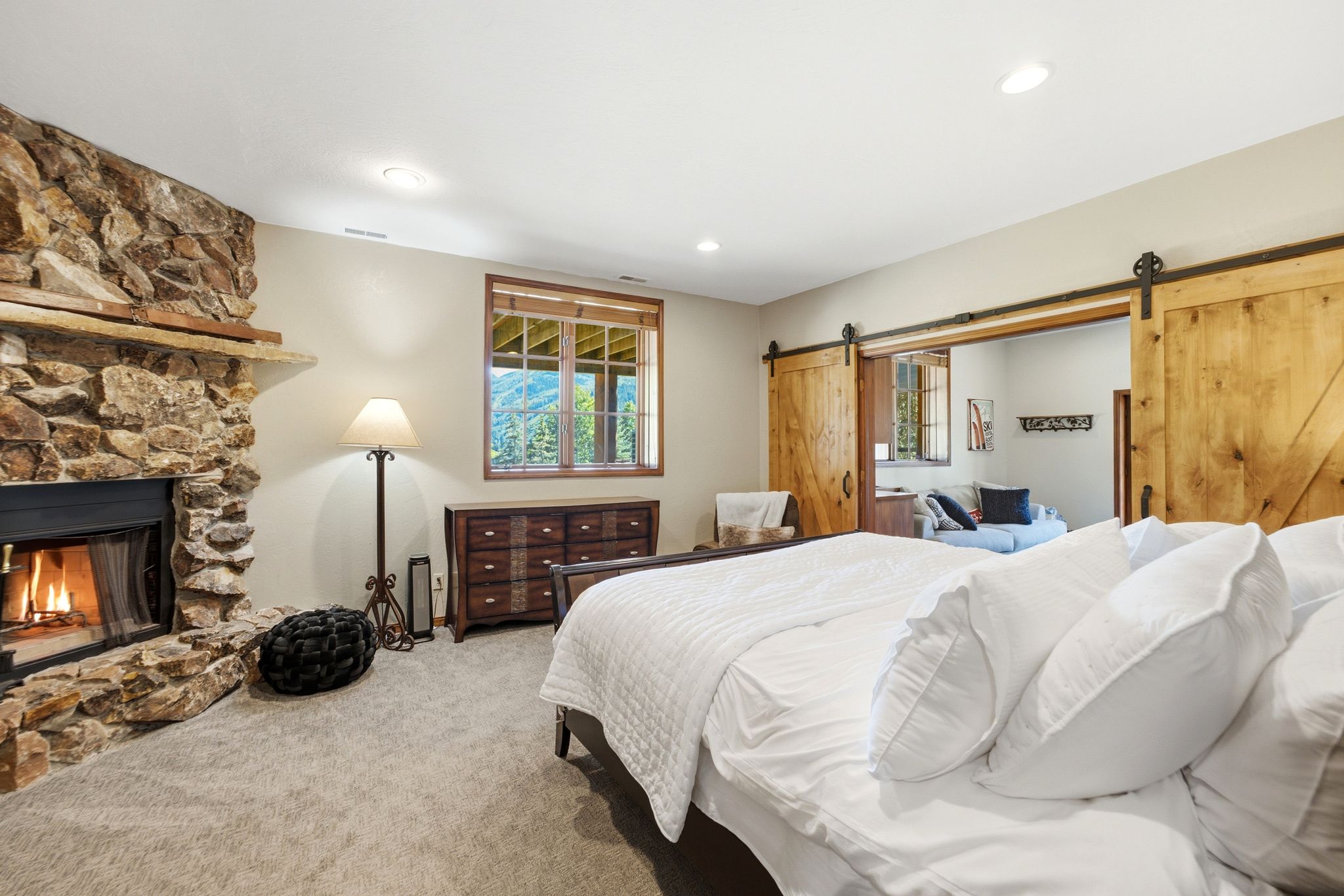Stone-clad fireplace with mantel, recessed lighting, carpeted flooring, and a large window with a wood-finish frame