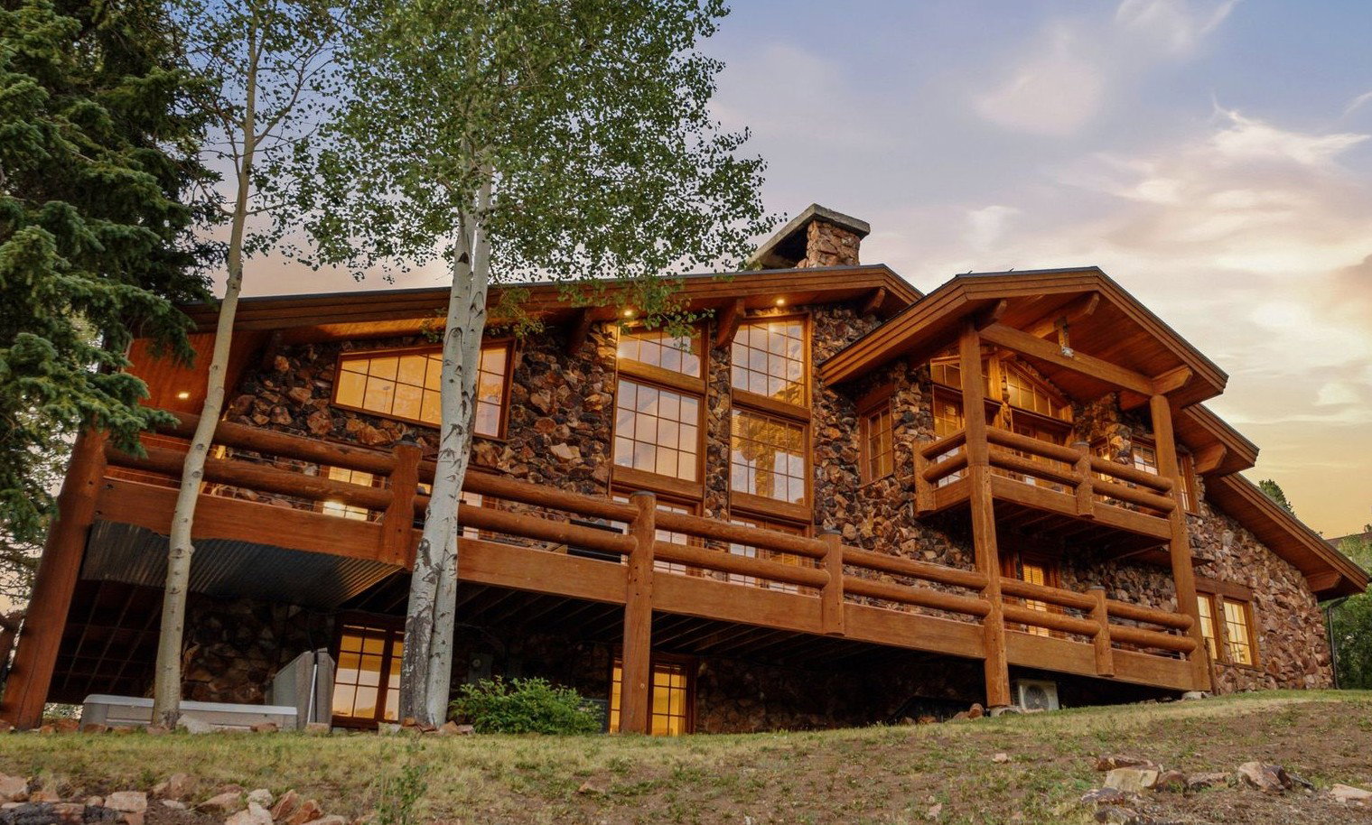 Rustic stone and log home featuring multiple balconies and extensive outdoor decking