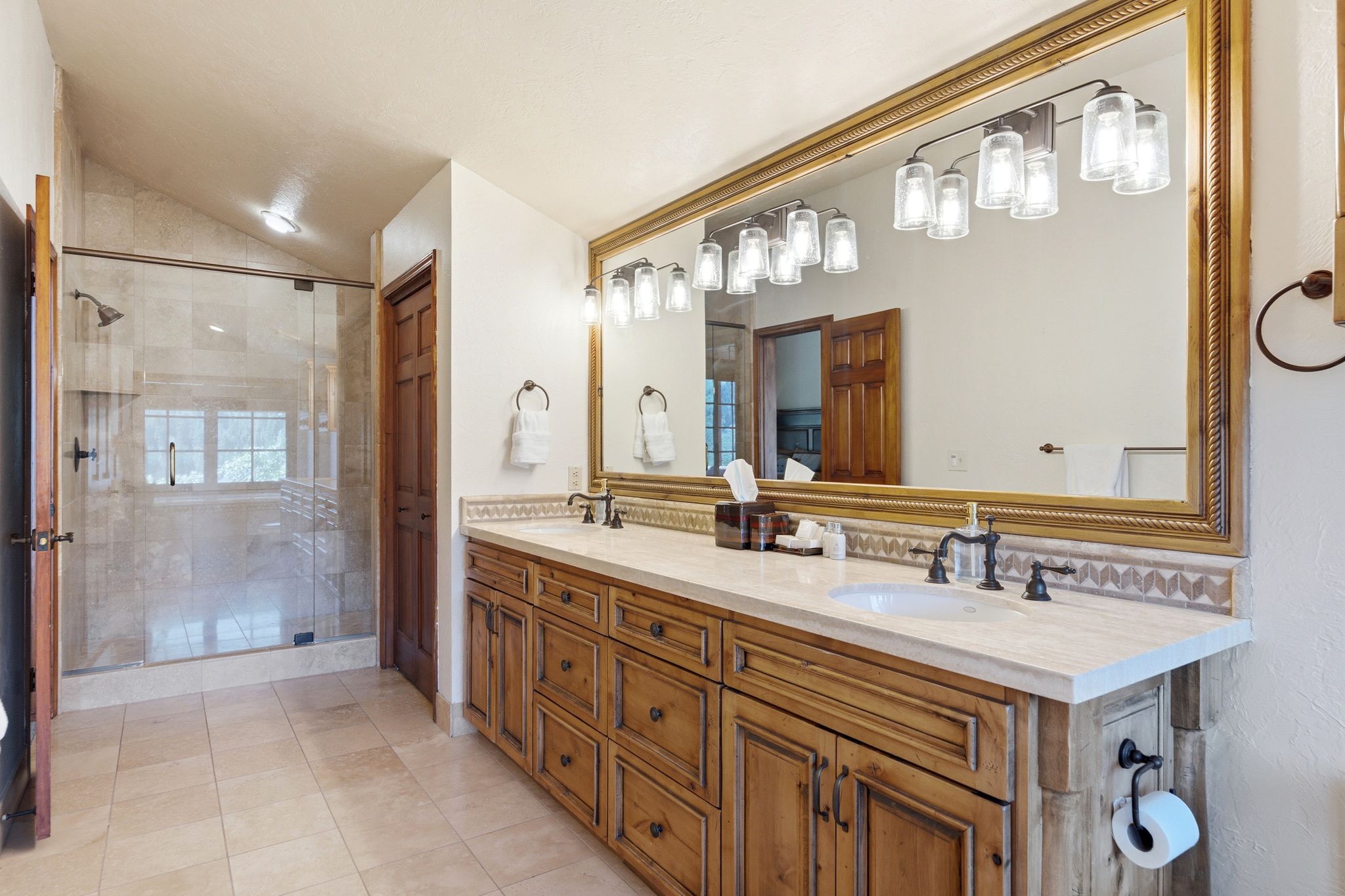 Dual vanity with natural wood-finish cabinetry, light-toned countertop, and a large framed mirror