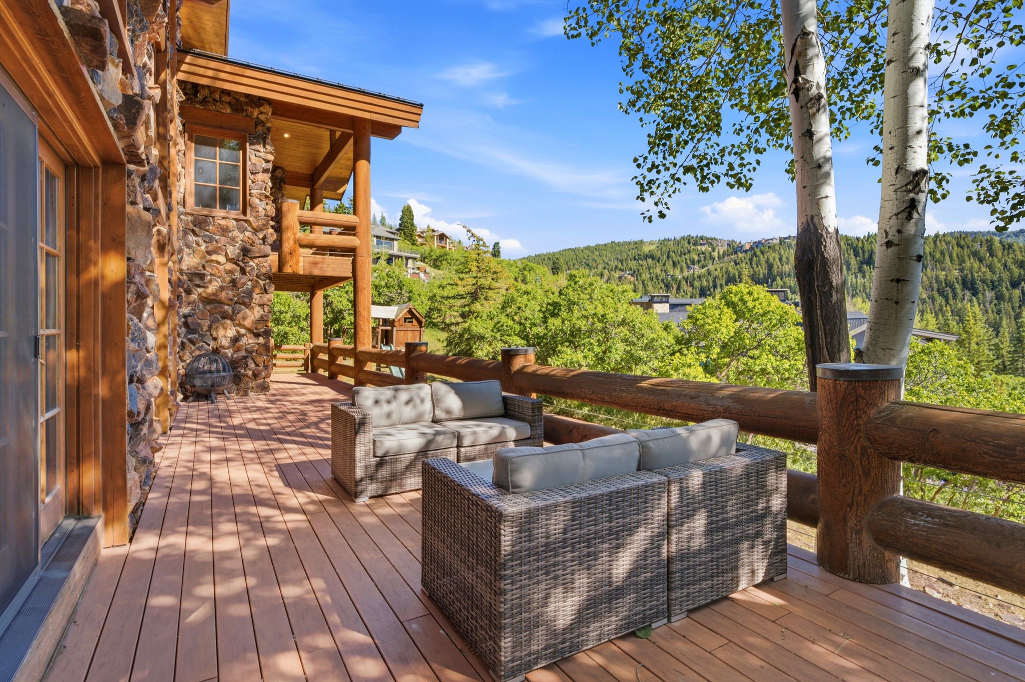 Spacious outdoor deck featuring wood-finish flooring, log railings, and a stone-clad exterior