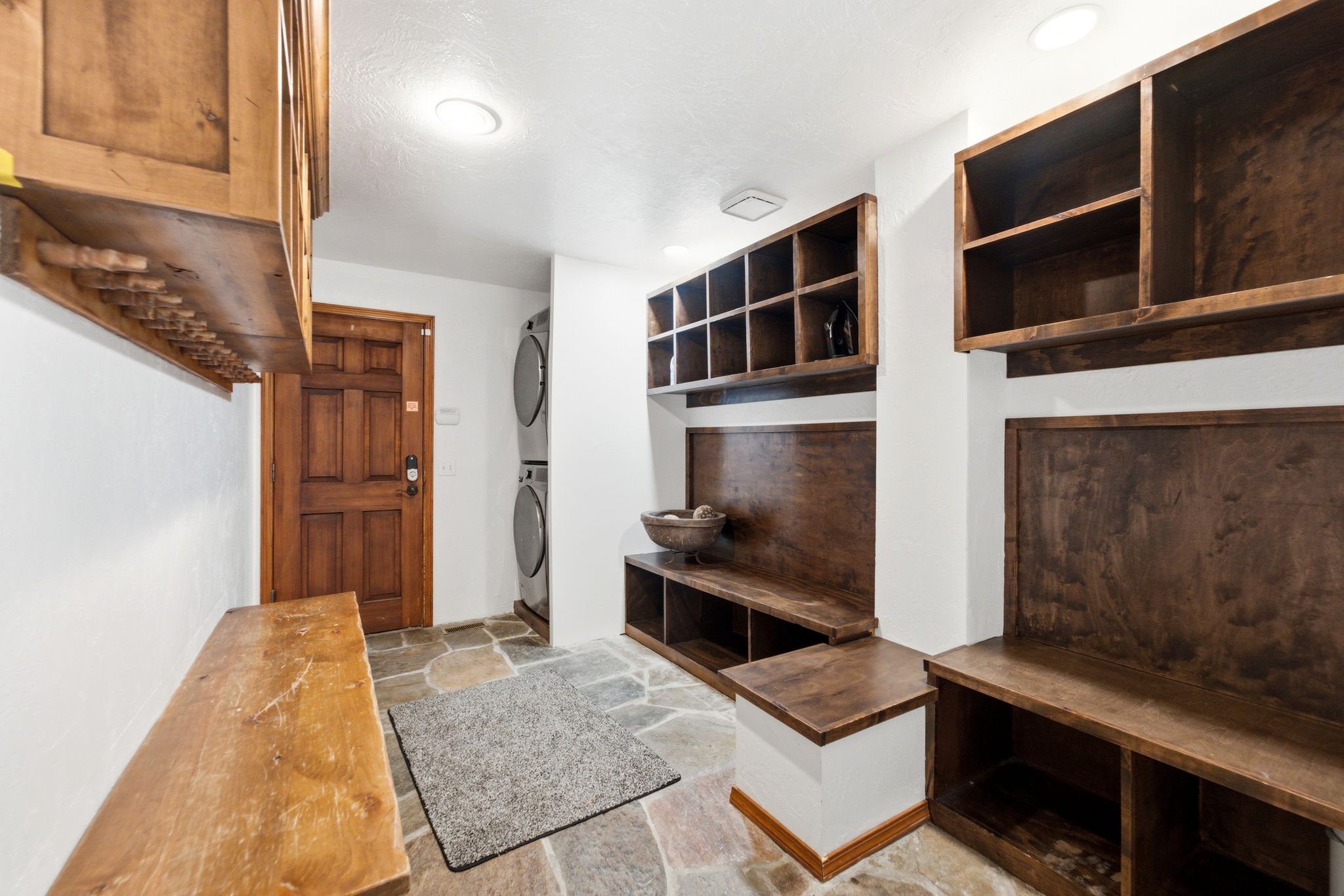Mudroom featuring stone flooring, built-in wooden cabinetry, integrated shelving, and a stacked washer and dryer unit