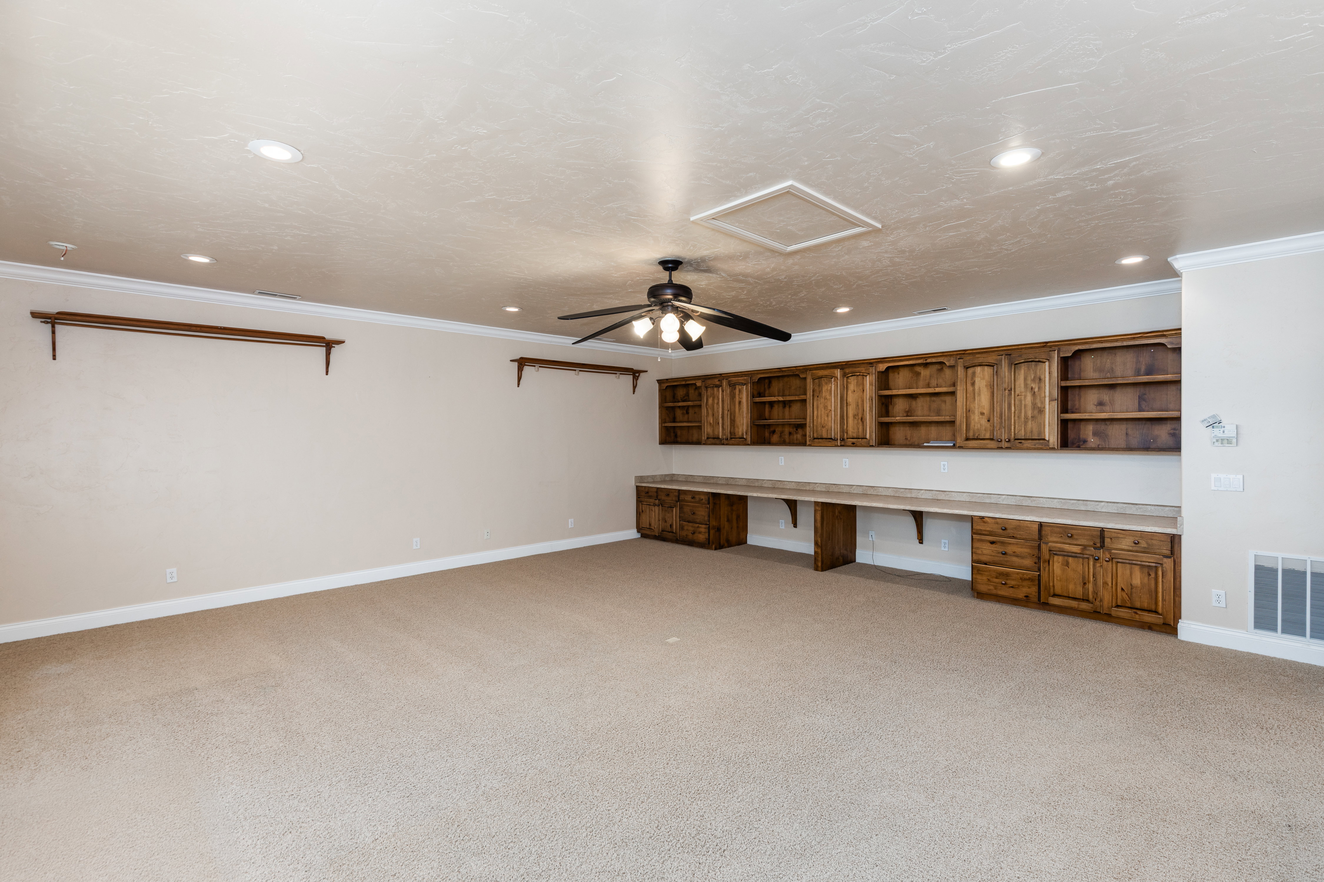 Spacious room featuring extensive built-in wooden cabinetry, integrated desk space, recessed ceiling lighting, a ceiling fan, and light-toned carpeting