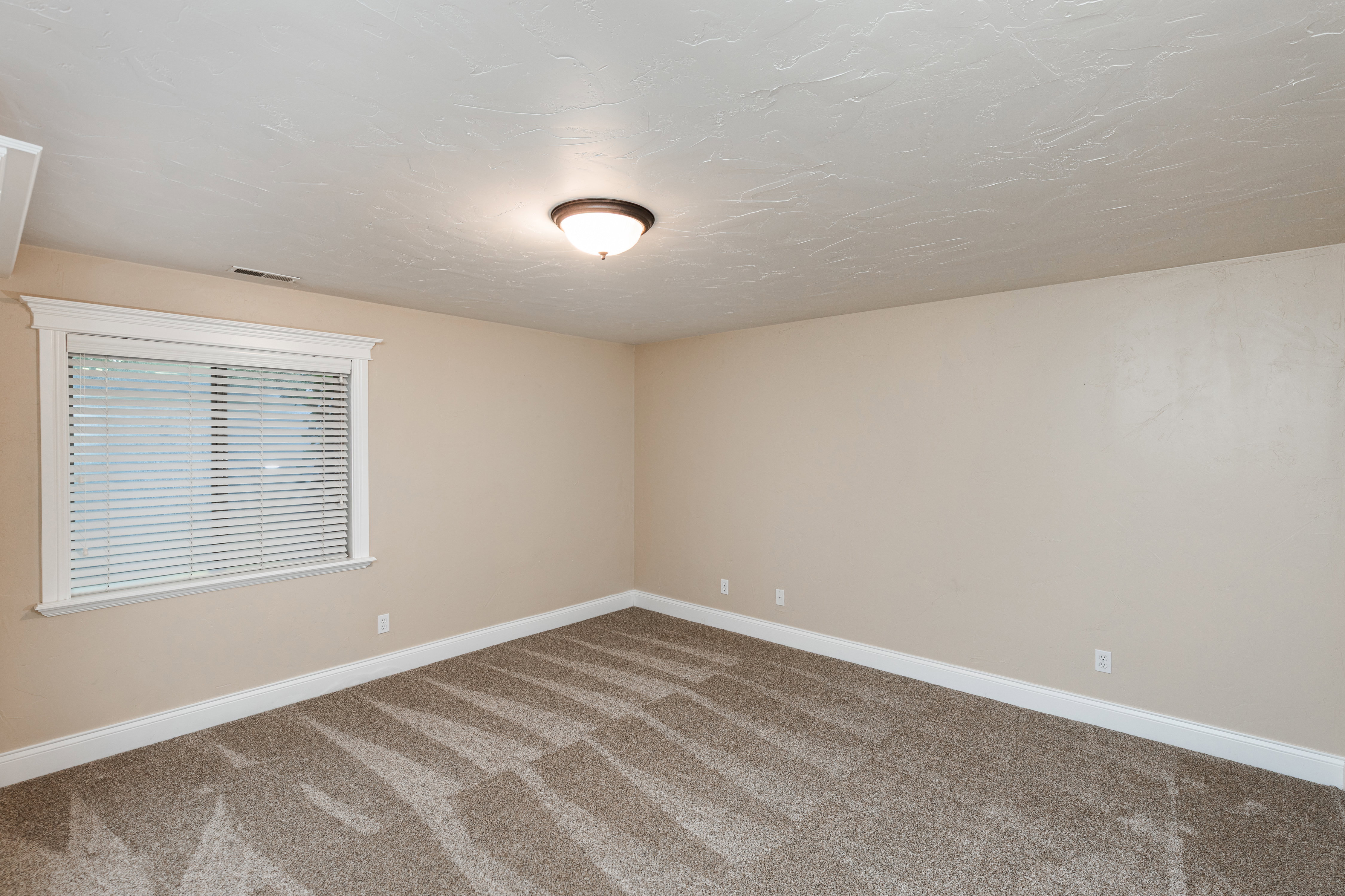 Spacious room featuring neutral paint, textured ceiling, patterned carpet, and a window with white trim and blinds