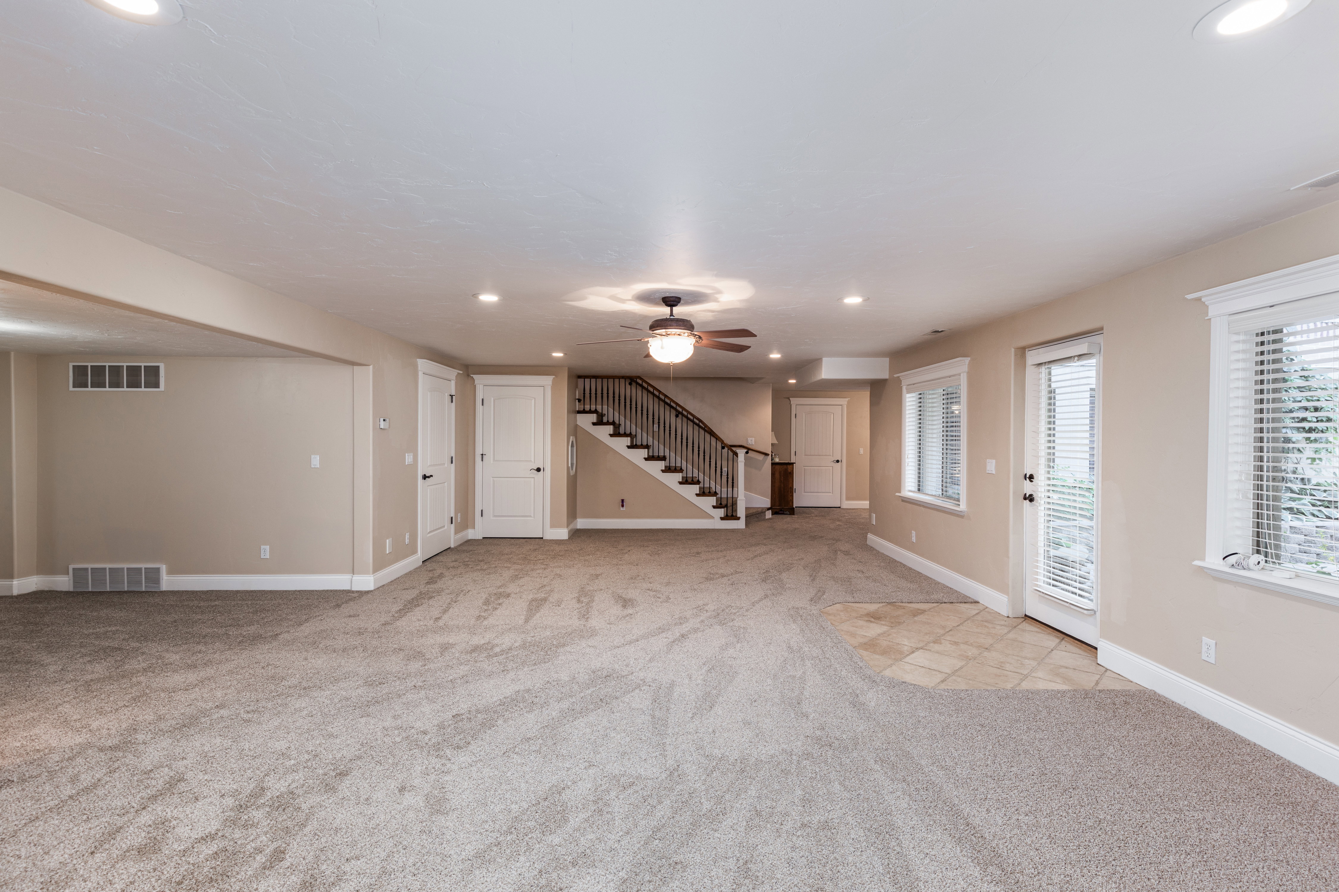 Spacious open area featuring neutral-toned carpeting, recessed lighting, and a ceiling fan