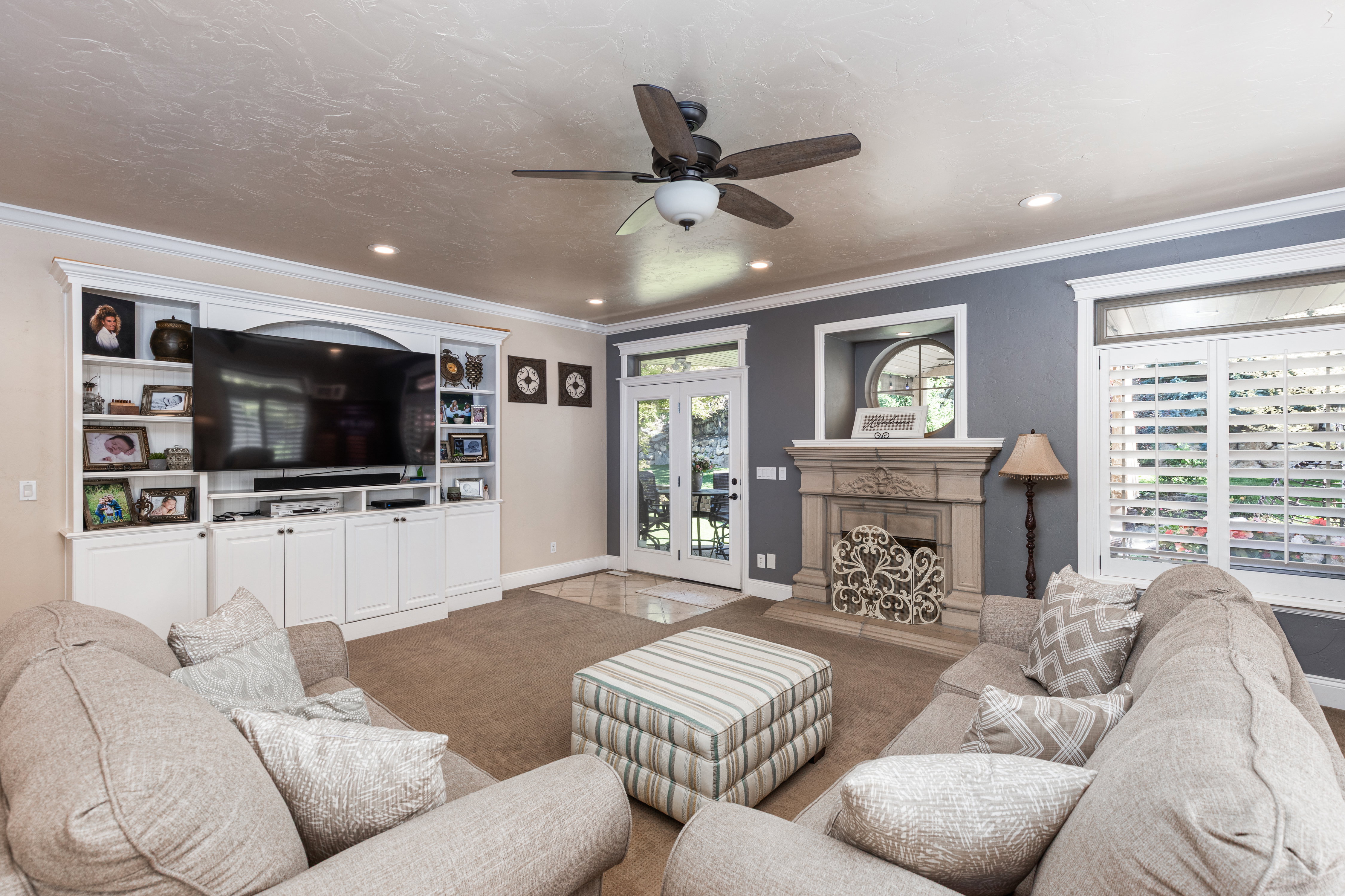 Spacious living area featuring a built-in entertainment center, a decorative fireplace with an ornate mantel, French doors, plantation shutters, and crown molding