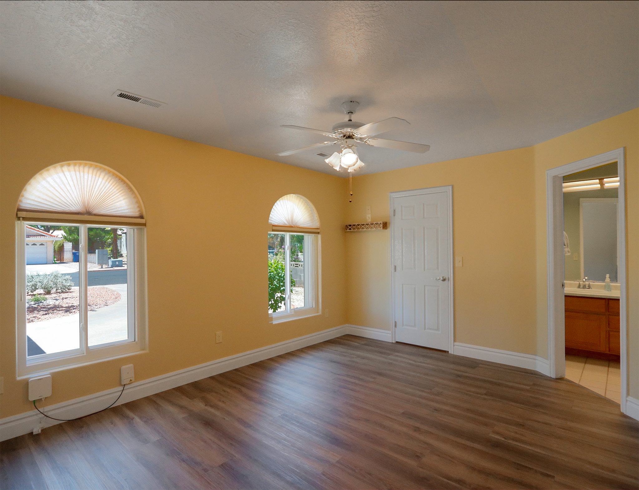 Spacious room featuring wood-finish flooring, two arched windows with pleated blinds, and a ceiling fan with integrated lighting