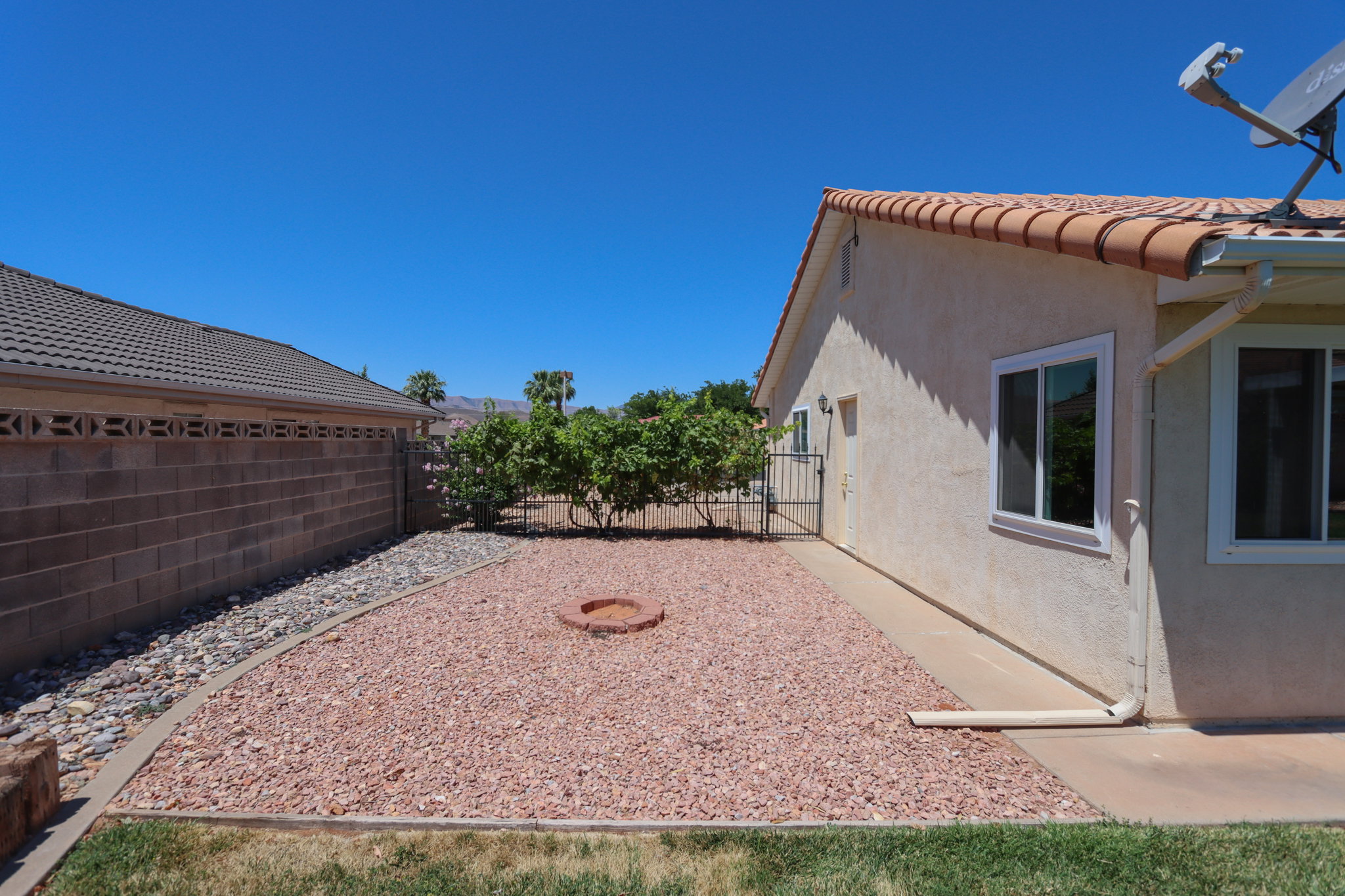 Low-maintenance backyard featuring xeriscaping with red gravel and river rock, a built-in fire pit, and a stucco exterior