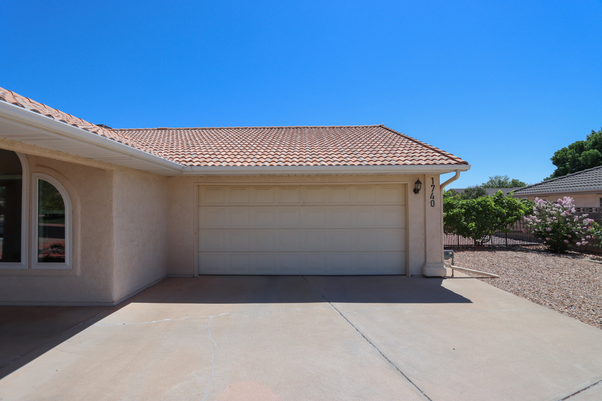 Stucco exterior with a tile roof, an integrated garage, a concrete driveway, and a rock landscaping bed with established plantings