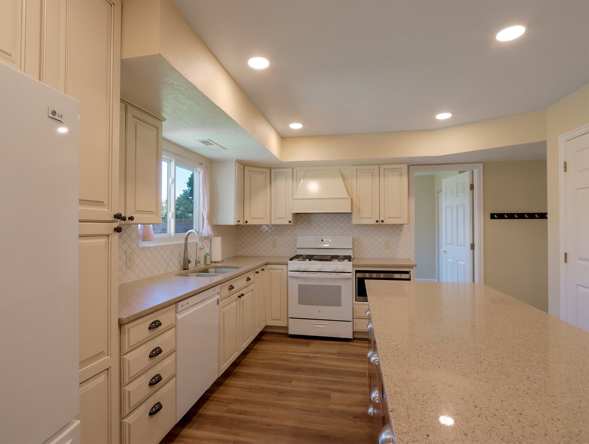 Spacious kitchen featuring an expansive island with a light-colored countertop, abundant cabinetry, wood-finish flooring, a white range with an overhead hood, and recessed lighting