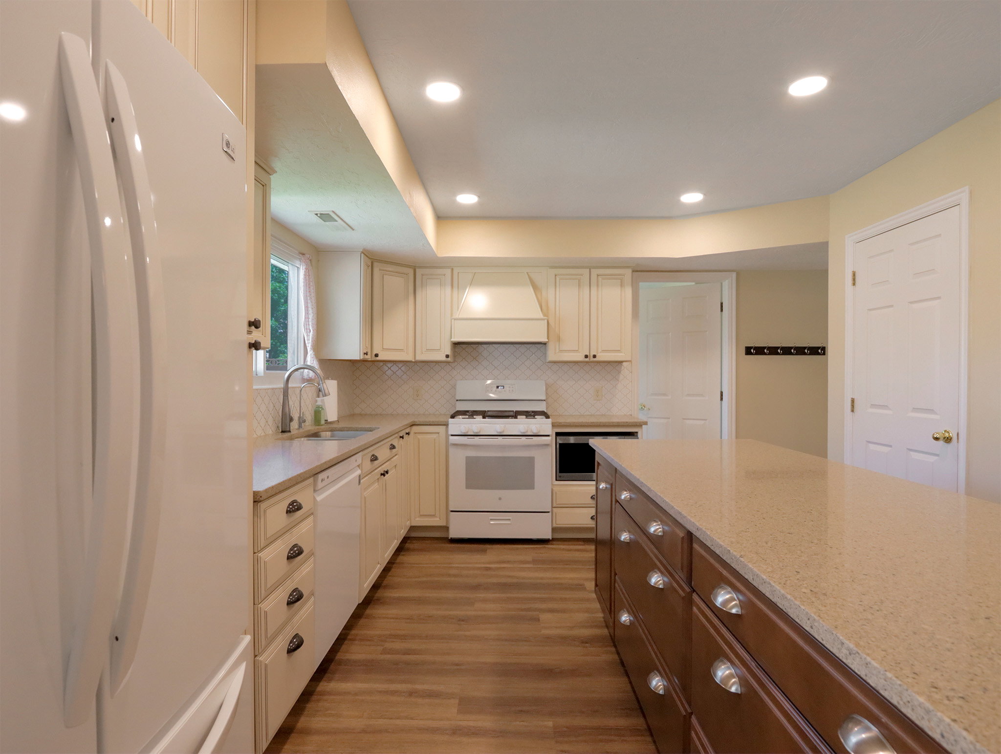 Kitchen featuring wood-finish flooring, recessed lighting, cream cabinetry, a white tile backsplash, and a brown island with a stone-finish countertop