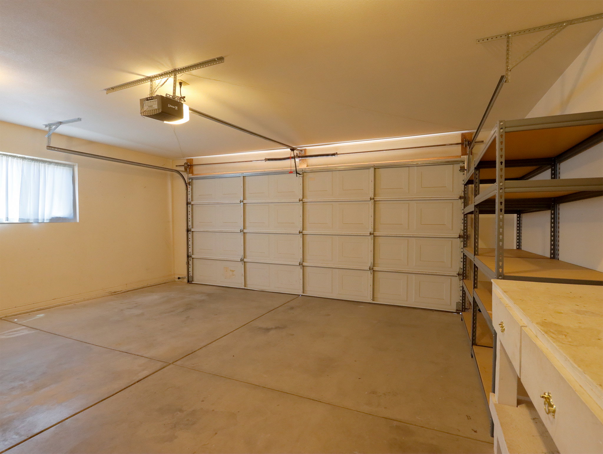 Spacious garage featuring a concrete floor, overhead lighting, a garage door opener, a window with curtains, and built-in metal shelving