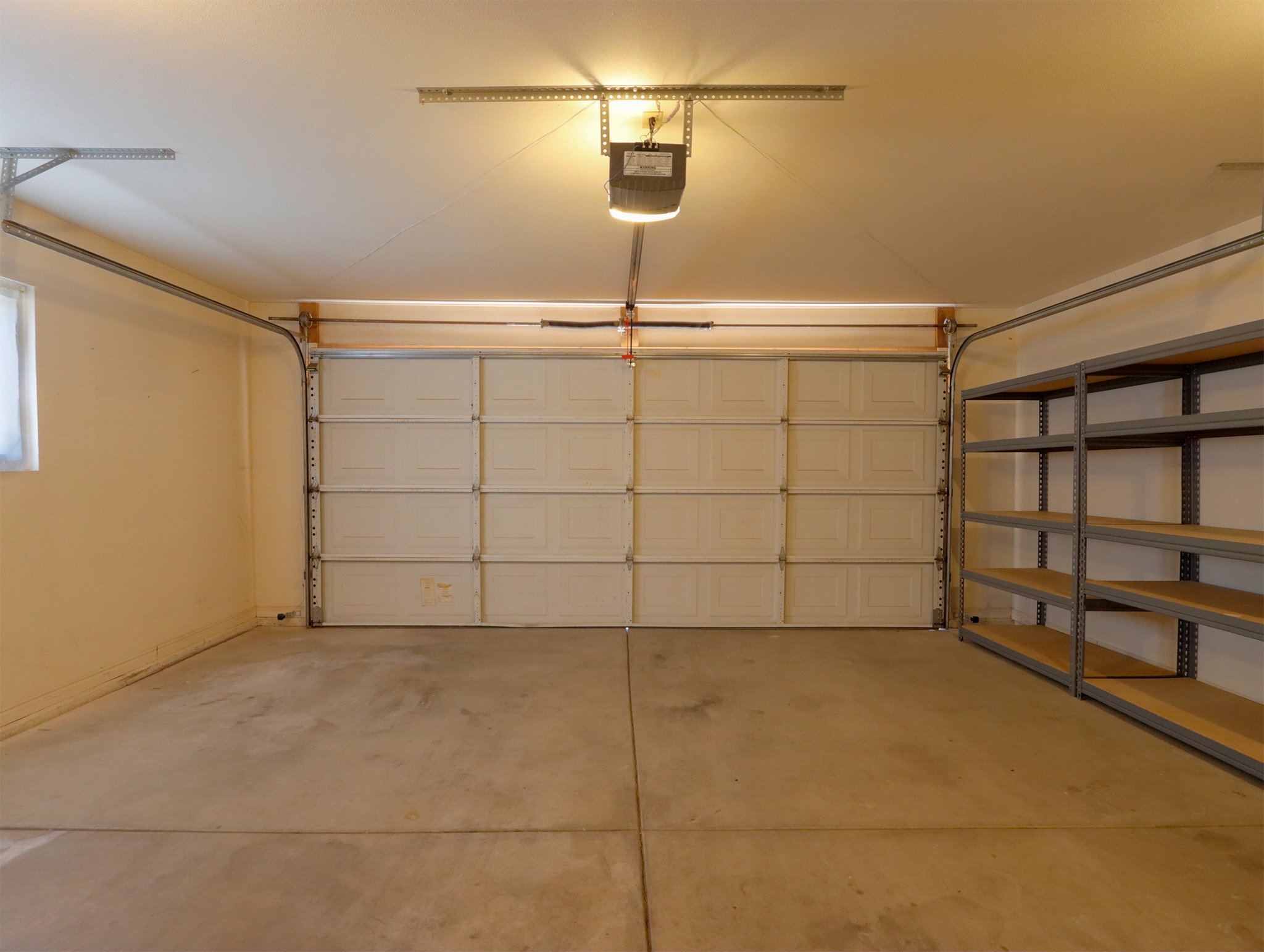 Spacious garage featuring a sectional garage door, concrete flooring, overhead lighting, and built-in shelving units