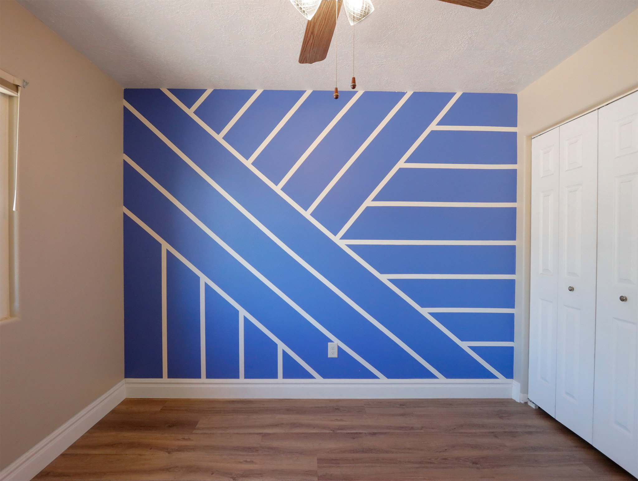 Feature wall with a geometric pattern in blue and white, wood-finish flooring, white baseboards, and a ceiling fan