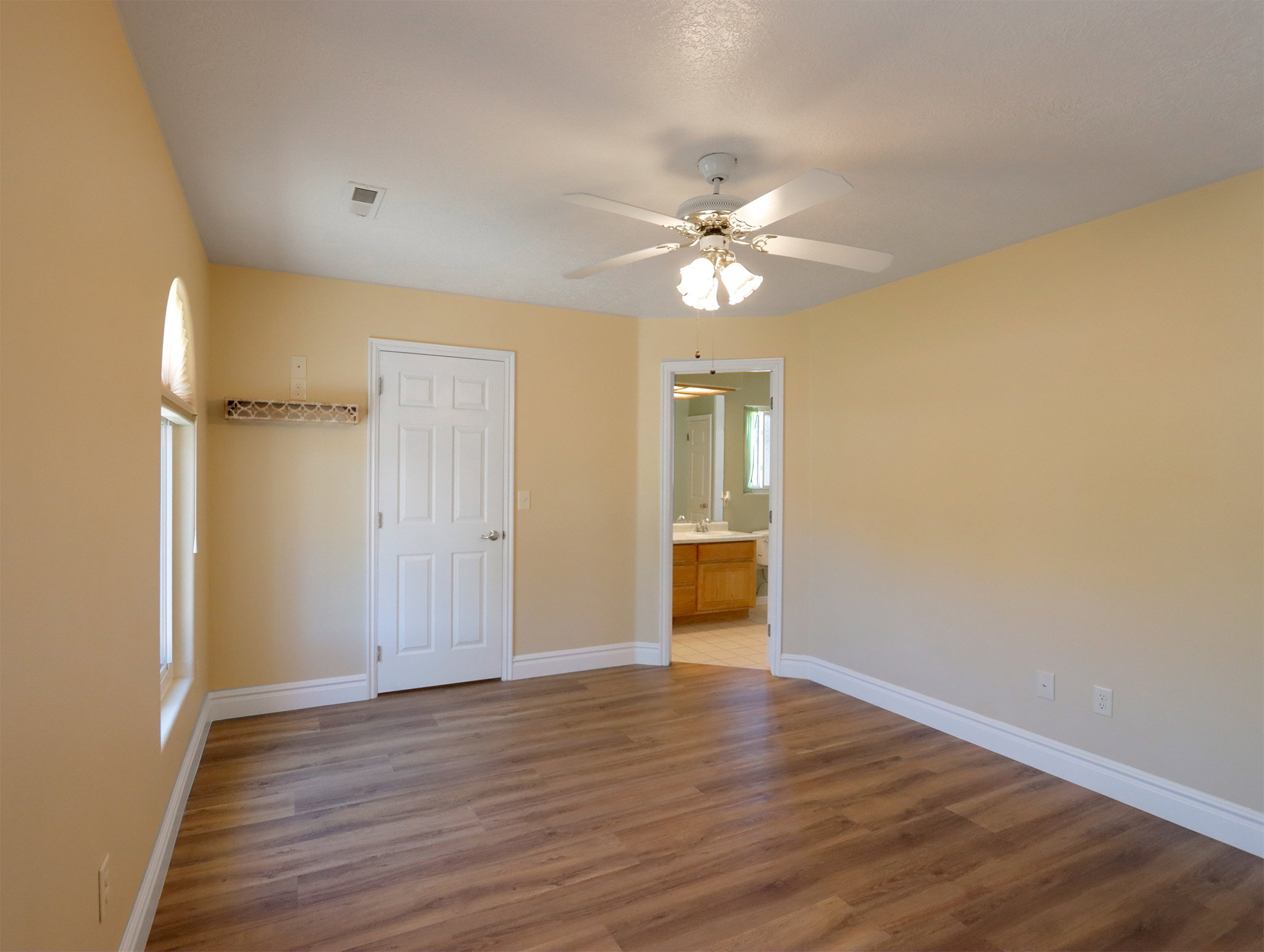 Spacious room featuring wood-finish flooring, light-toned walls, and a ceiling fan with integrated lighting
