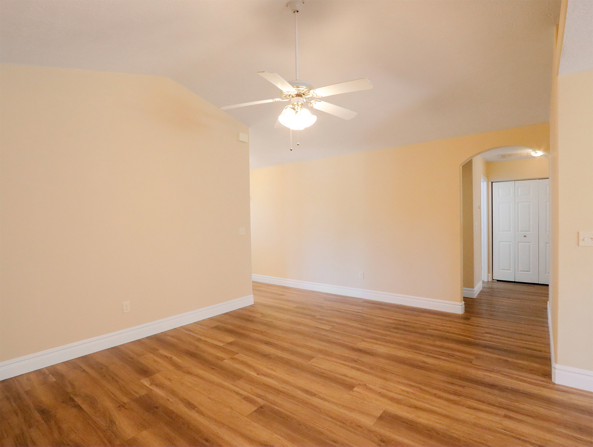 Spacious interior featuring wood-finish flooring, vaulted ceilings, and a ceiling fan with light fixture