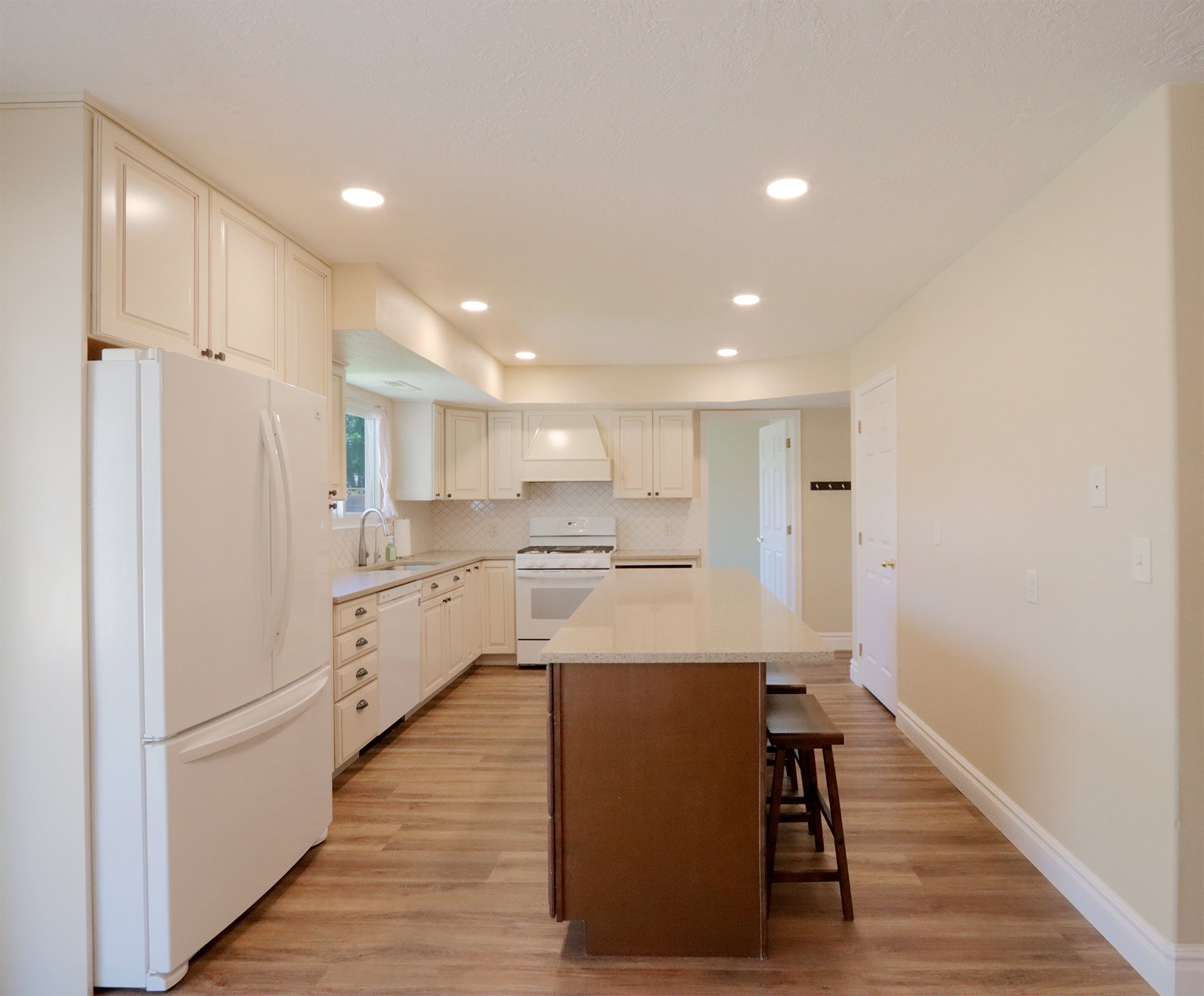 Bright kitchen with white cabinetry, wood-finish flooring, recessed lighting, a center island with countertop seating, and a white tile backsplash