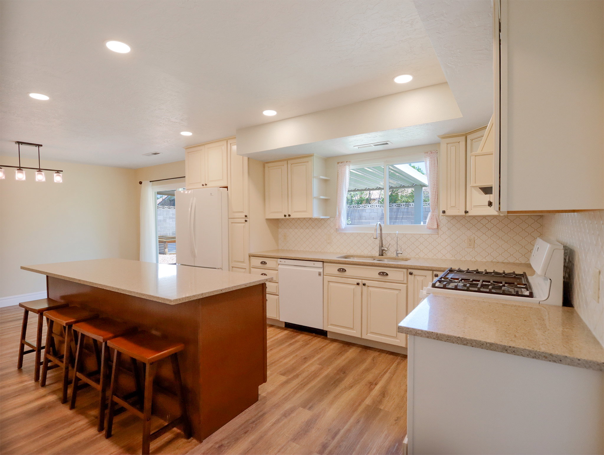Kitchen featuring a large island with a light-toned countertop, cream cabinetry, light wood-finish flooring, recessed lighting, and a patterned tile backsplash