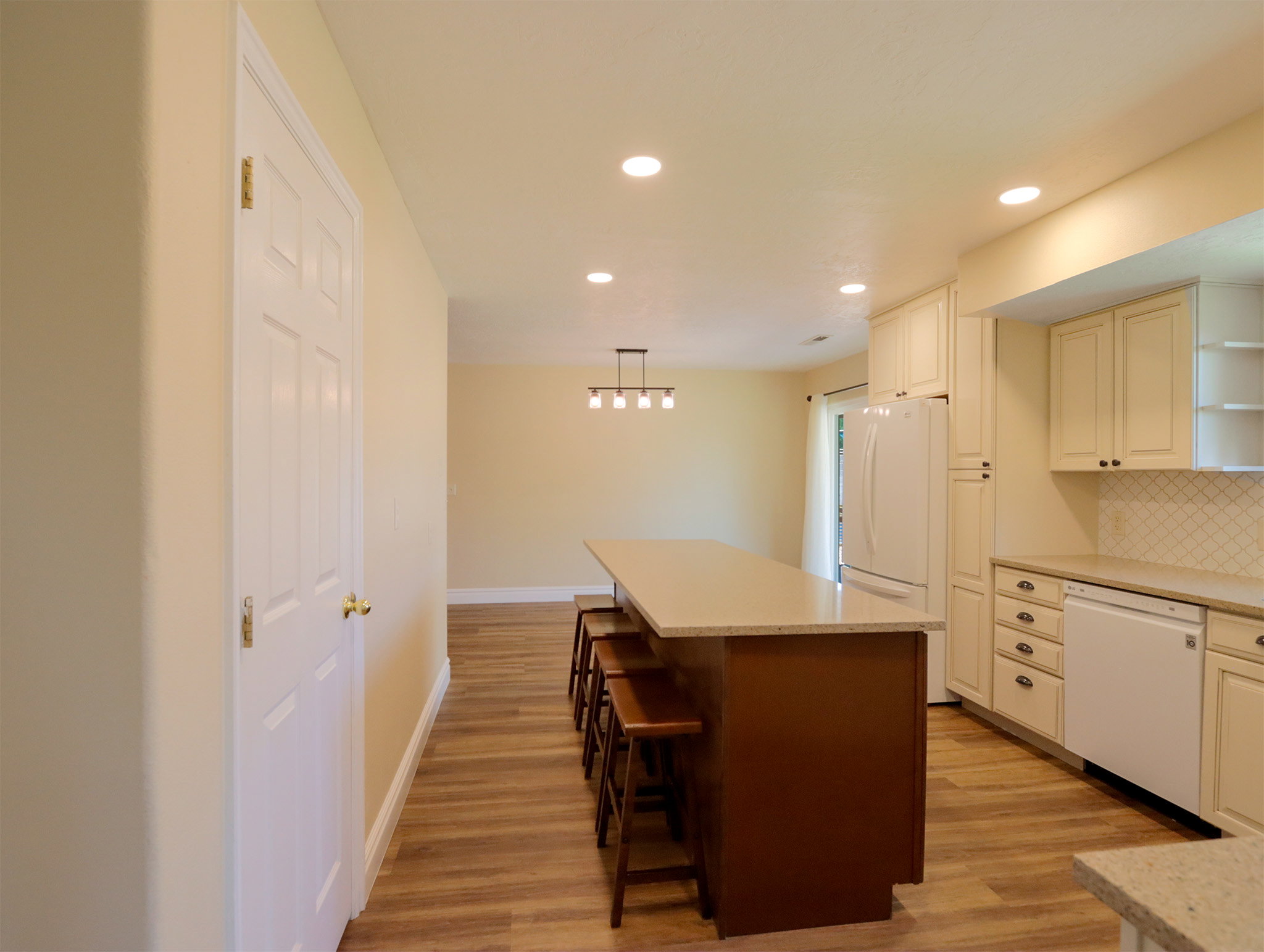 Kitchen featuring an elongated island with a light-toned countertop, white cabinetry with dark hardware, recessed lighting, wood-finish flooring, and a white tile backsplash